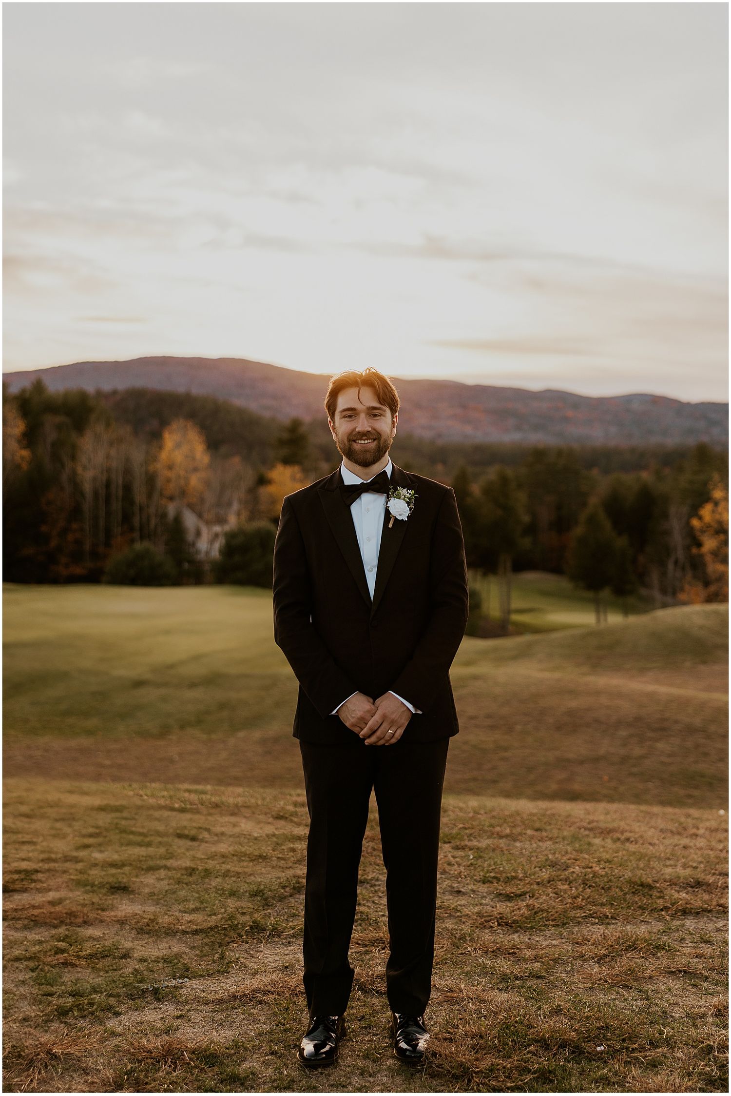 A formal portrait in a black tuxedo against rolling hills at golden hour.