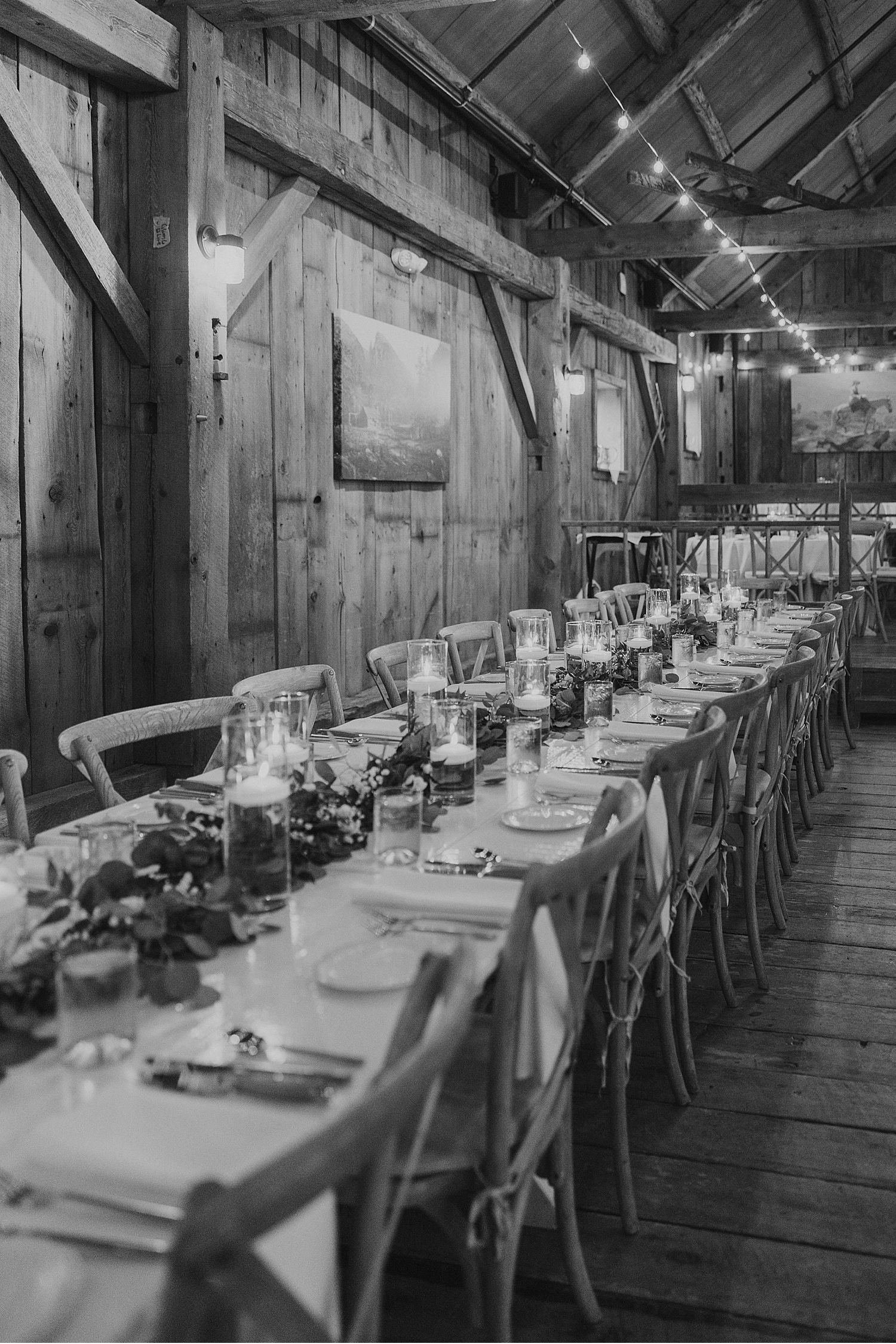 Long rustic wooden dining tables set for a wedding reception with white linens and place settings.