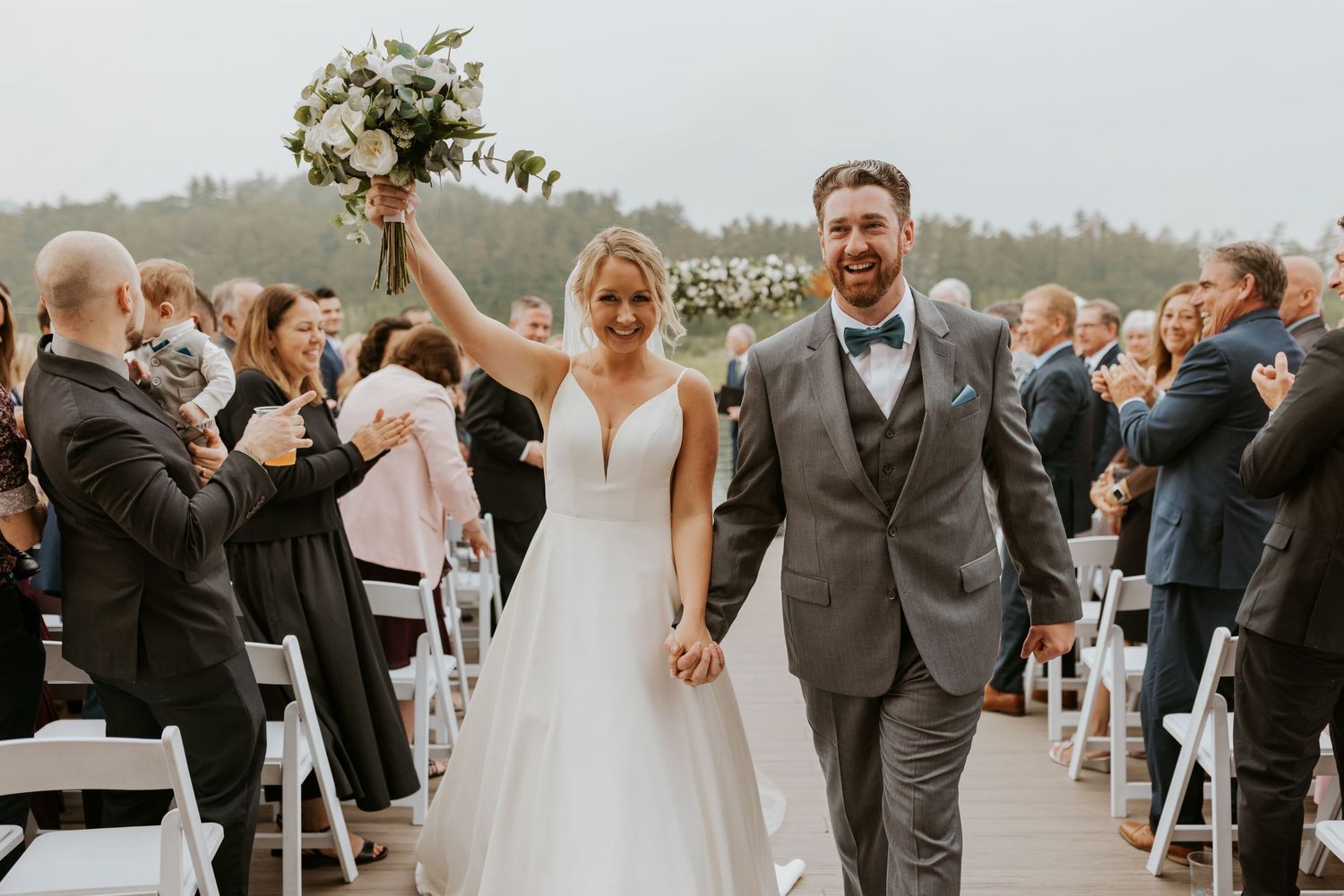 Bride and groom walk back down aisle celebrating after outdoor waterfront wedding ceremony.