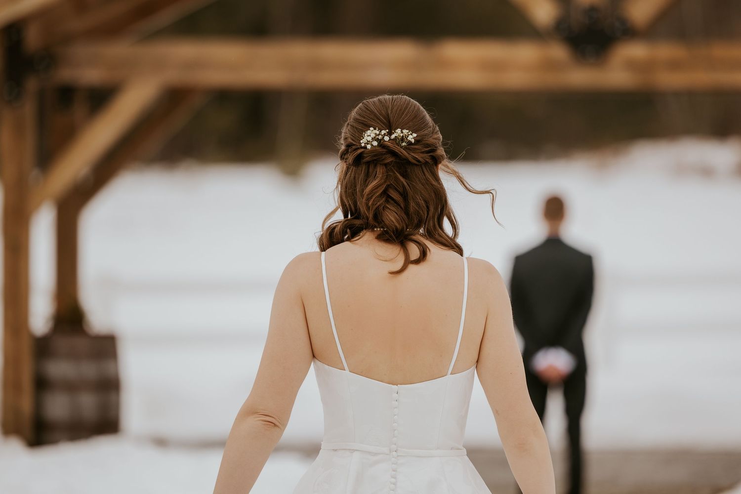Wedding couple walking through snow outside a rustic wooden barn venue during a winter ceremony.