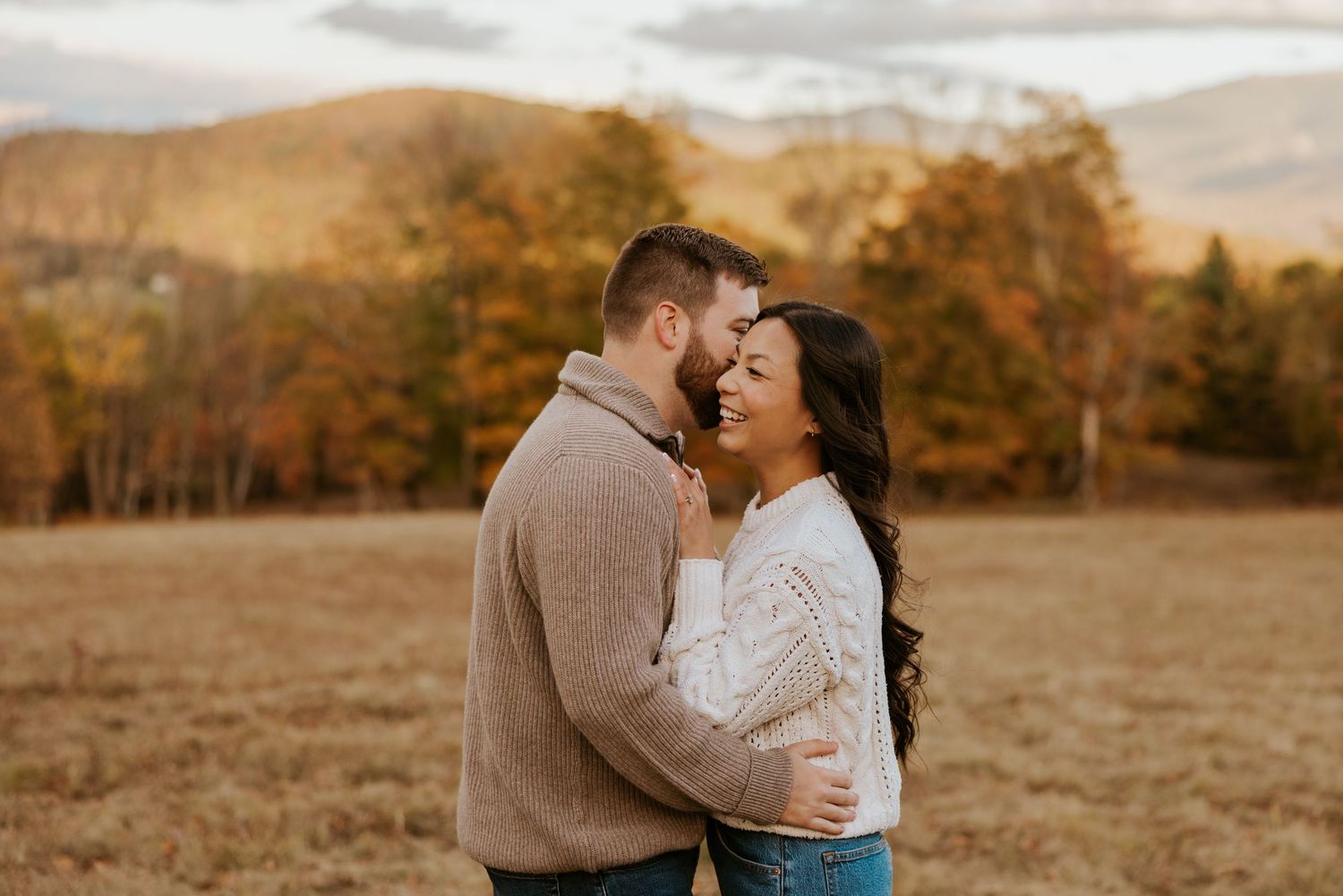Joyful couple laughing together in an open field with autumn mountains behind.
