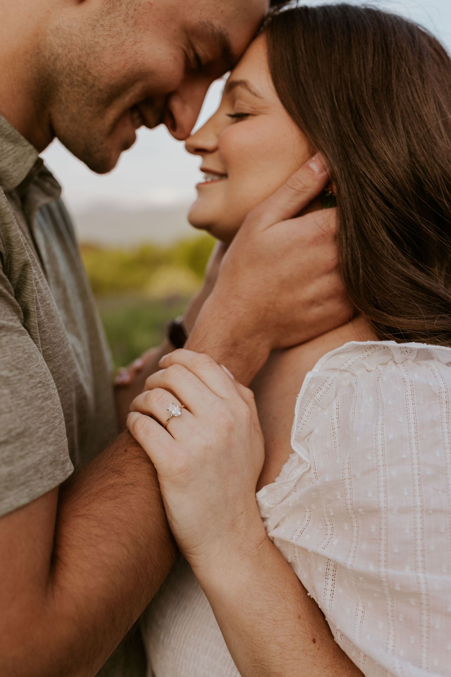 Close-up of an engaged couple touching foreheads, woman displaying a sparkling diamond ring.