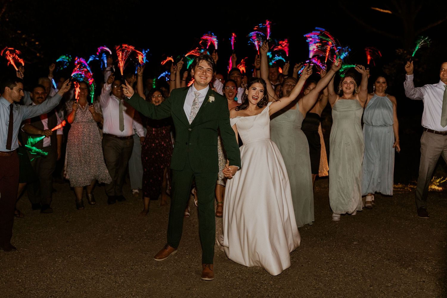 Wedding party dancing with colorful light sticks during nighttime reception.