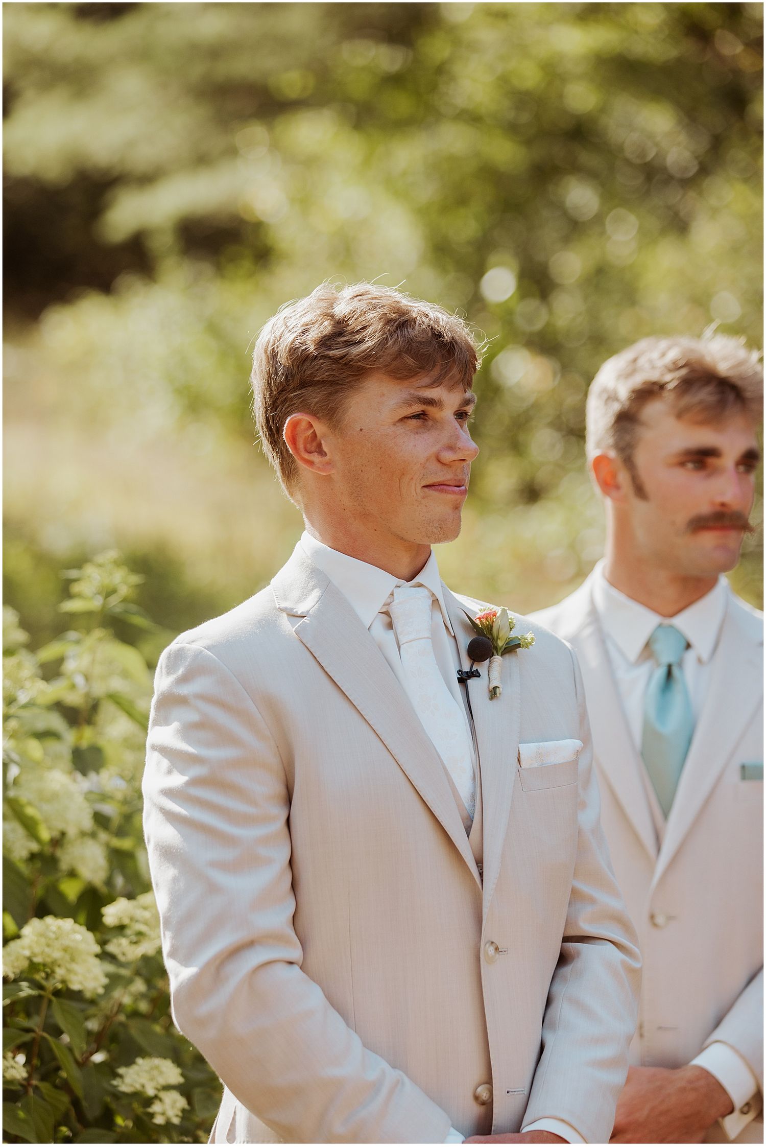 Groomsmen in light beige suits with mint green accents stand together in an outdoor garden setting.