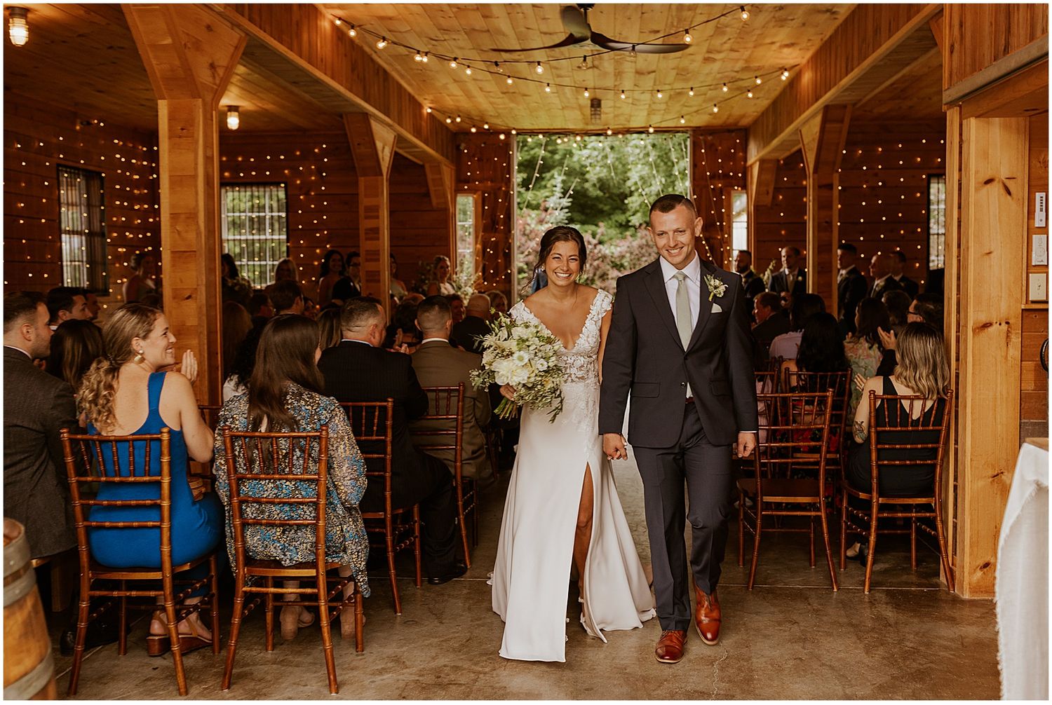 Wedding reception in a wooden barn venue with string lights and guests seated at tables.