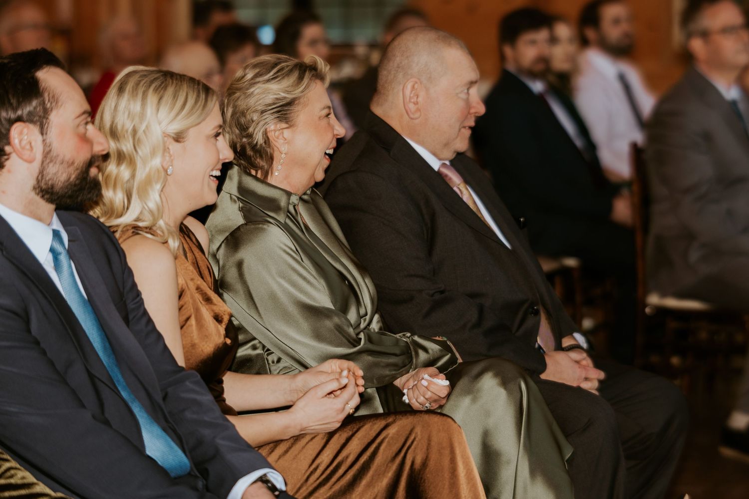 Wedding guests seated in formal attire watching the ceremony in an indoor venue.