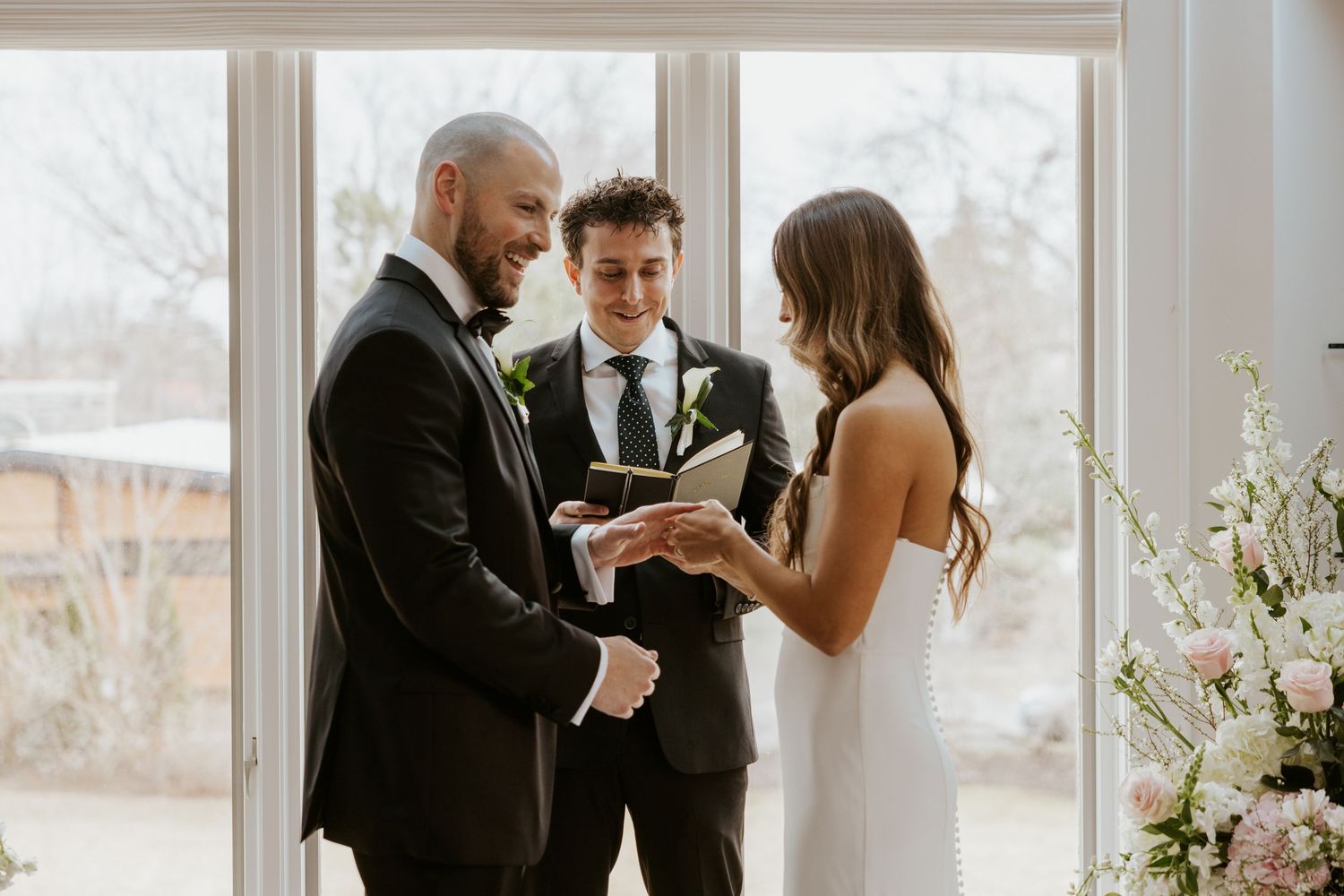 A wedding couple shares an intimate moment in a bright sunlit room with white floral decorations.
