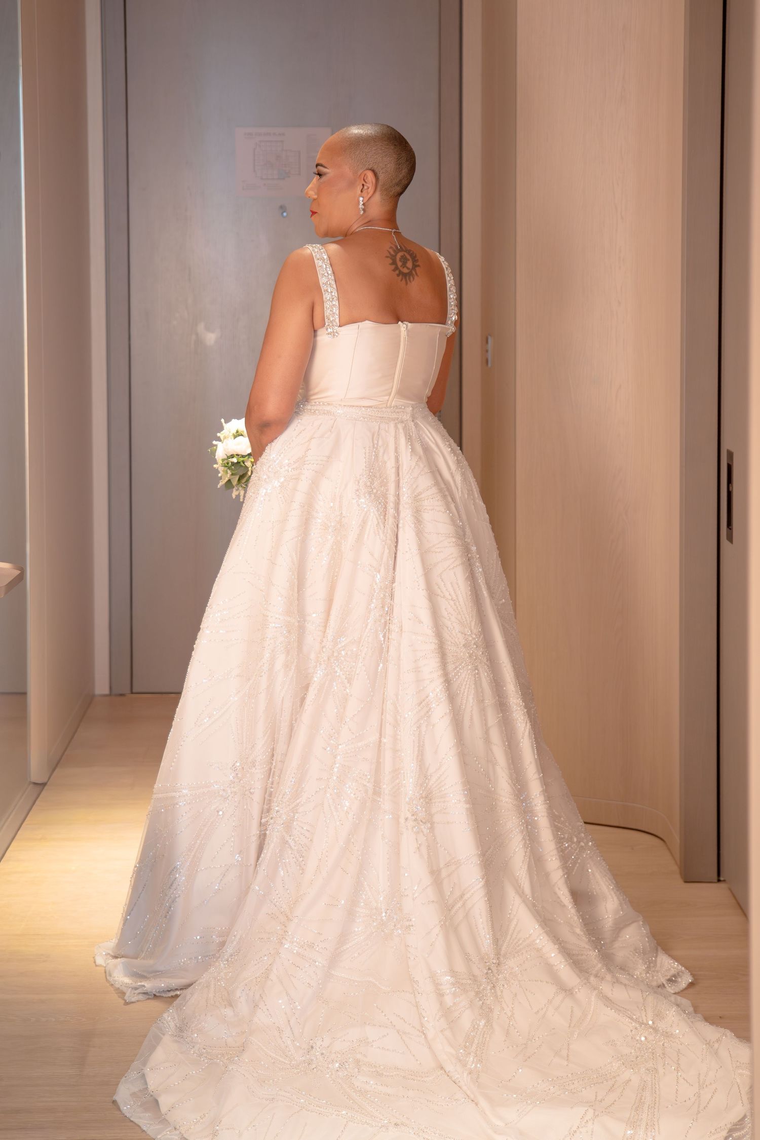 Bride in elegant white ballgown wedding dress with lace details, holding bouquet, viewed from behind.