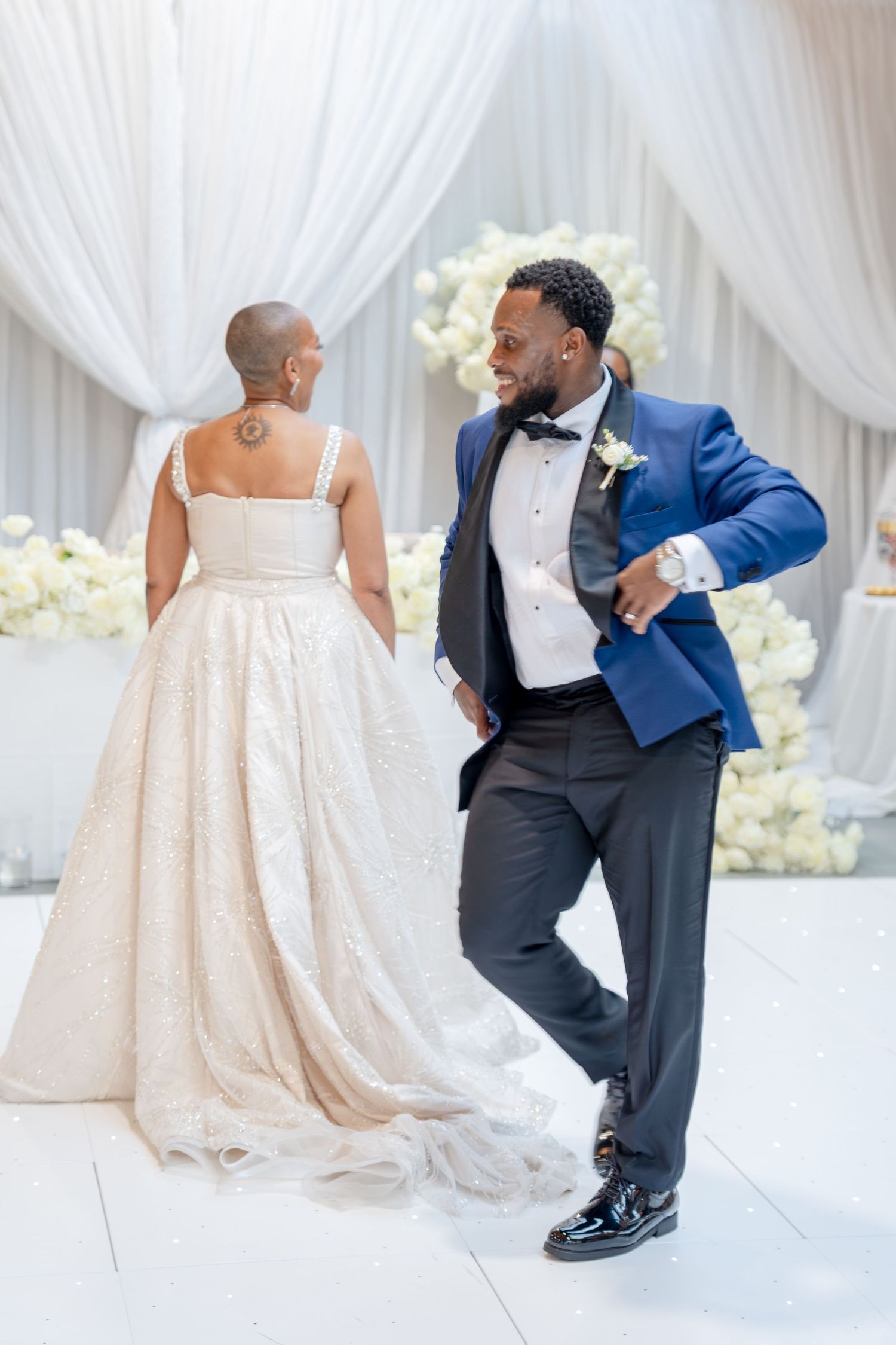 Bride and groom share a joyful first dance, she in a champagne gown, he in a blue tuxedo, at an elegant wedding reception.