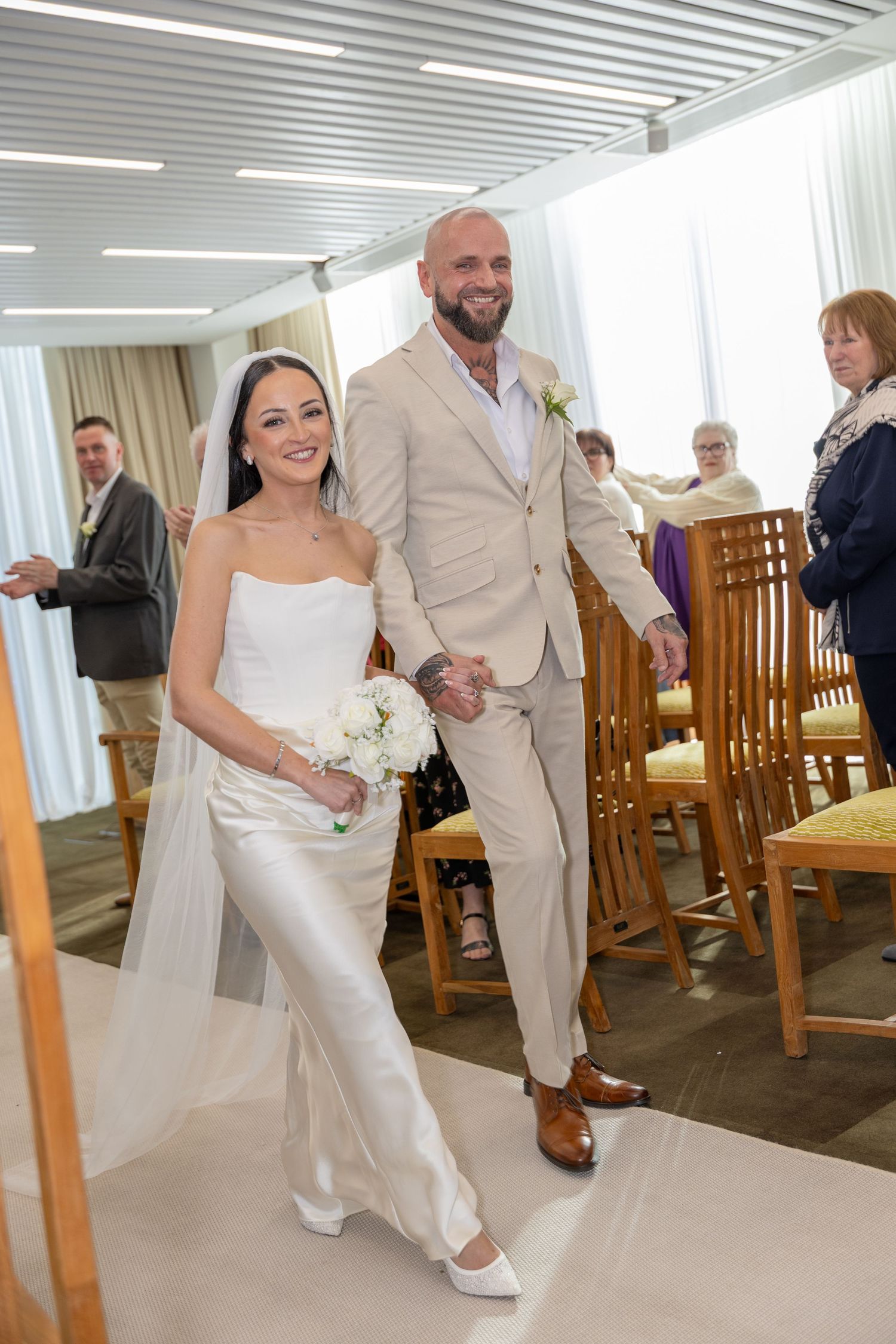 Happy couple walks up the aisle after wedding ceremony, guests applauding in the background.