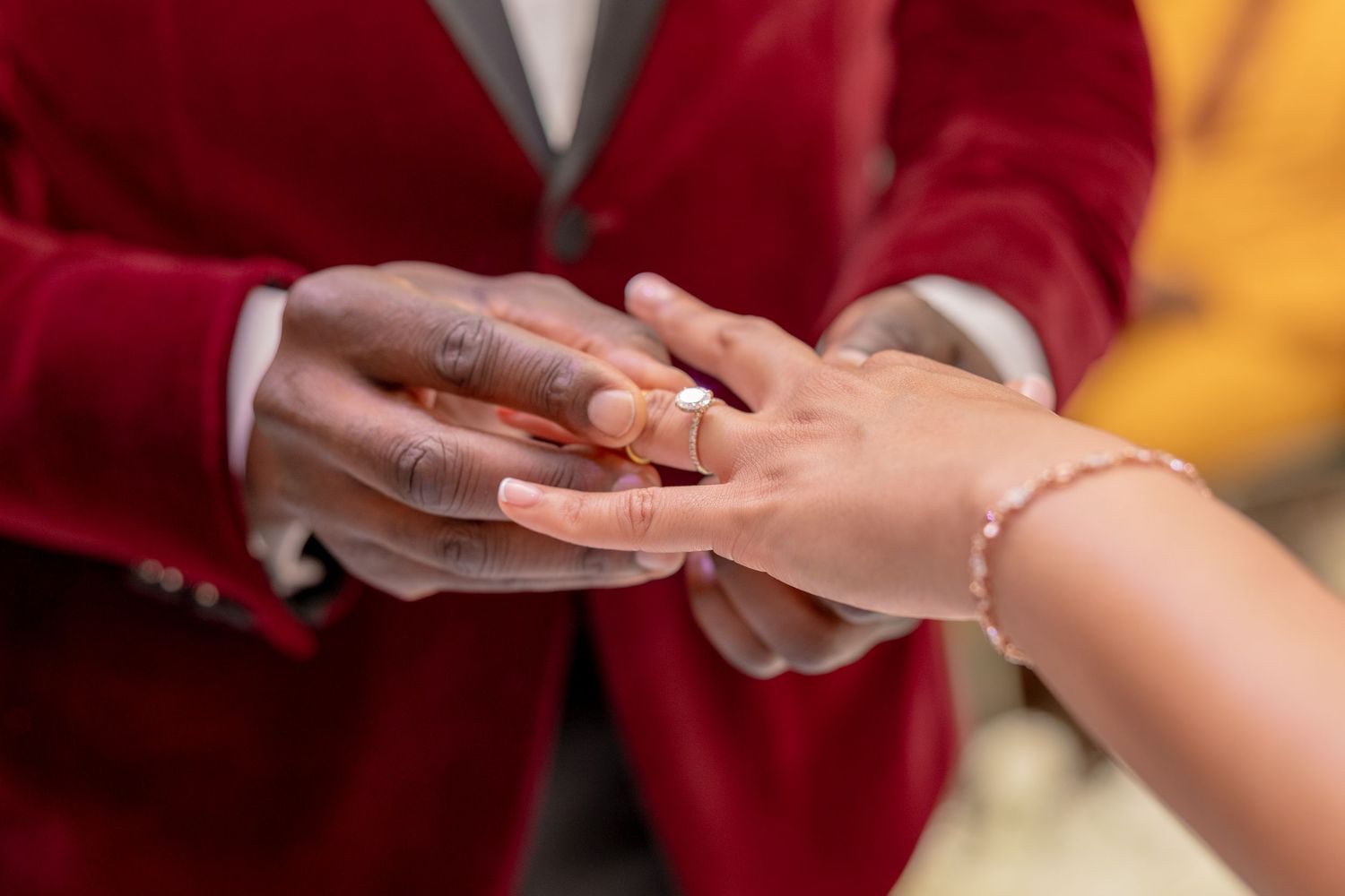 Close-up of a man placing a diamond ring on a woman's finger during a wedding ceremony.
