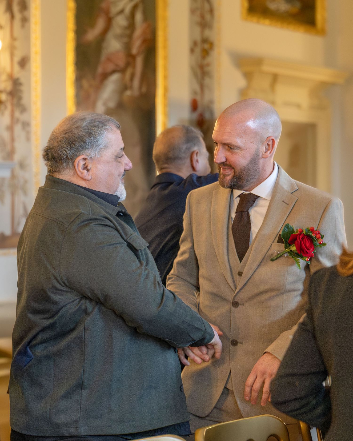 Two men in formal suits shaking hands at an elegant wedding reception venue.