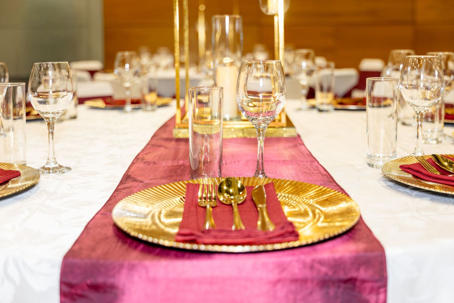 Luxurious wedding table setting with gold charger plates, burgundy velvet runner, and crystal glasses.
