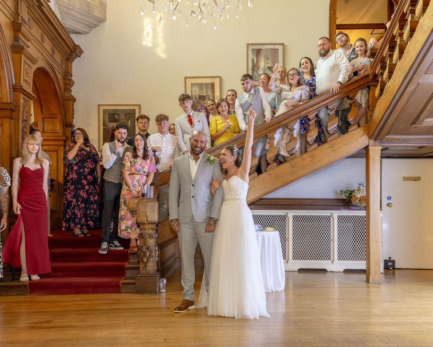 Bride tosses bouquet to guests gathered on grand staircase during elegant wedding reception in historic venue.