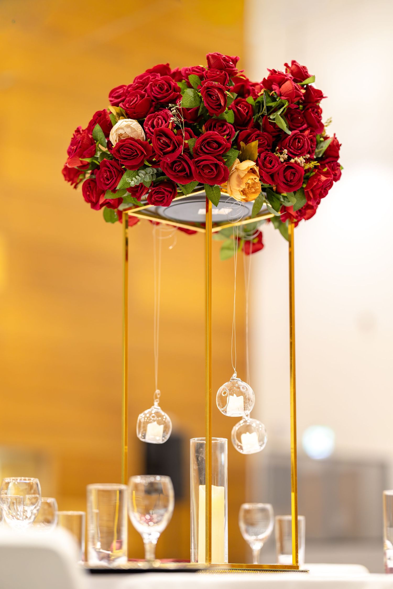 Elegant wedding centerpiece with red roses on a gold stand with hanging crystal globes.