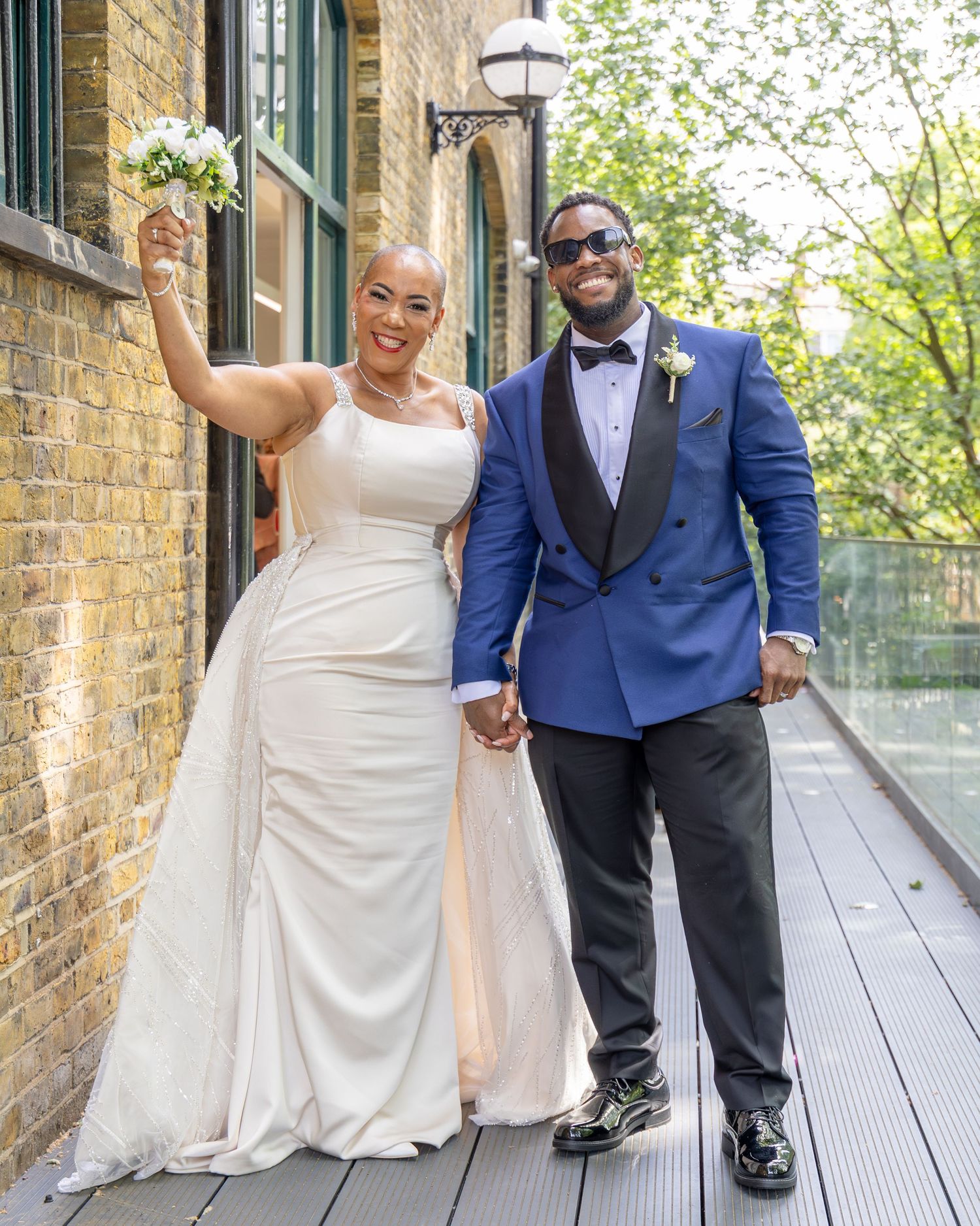 A joyful bride in a white gown and groom in a blue tuxedo hold hands and celebrate on their wedding day.
