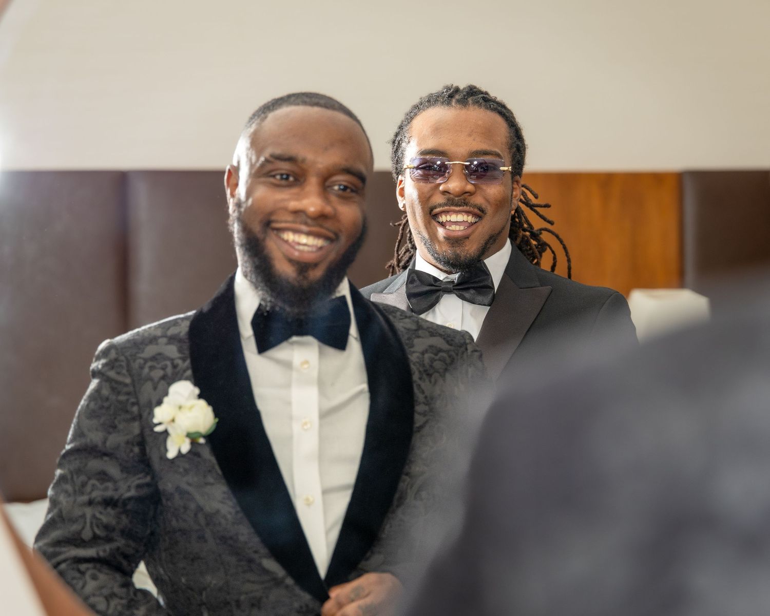 Two well-dressed men in matching patterned tuxedos with bow ties smiling together at a formal event.