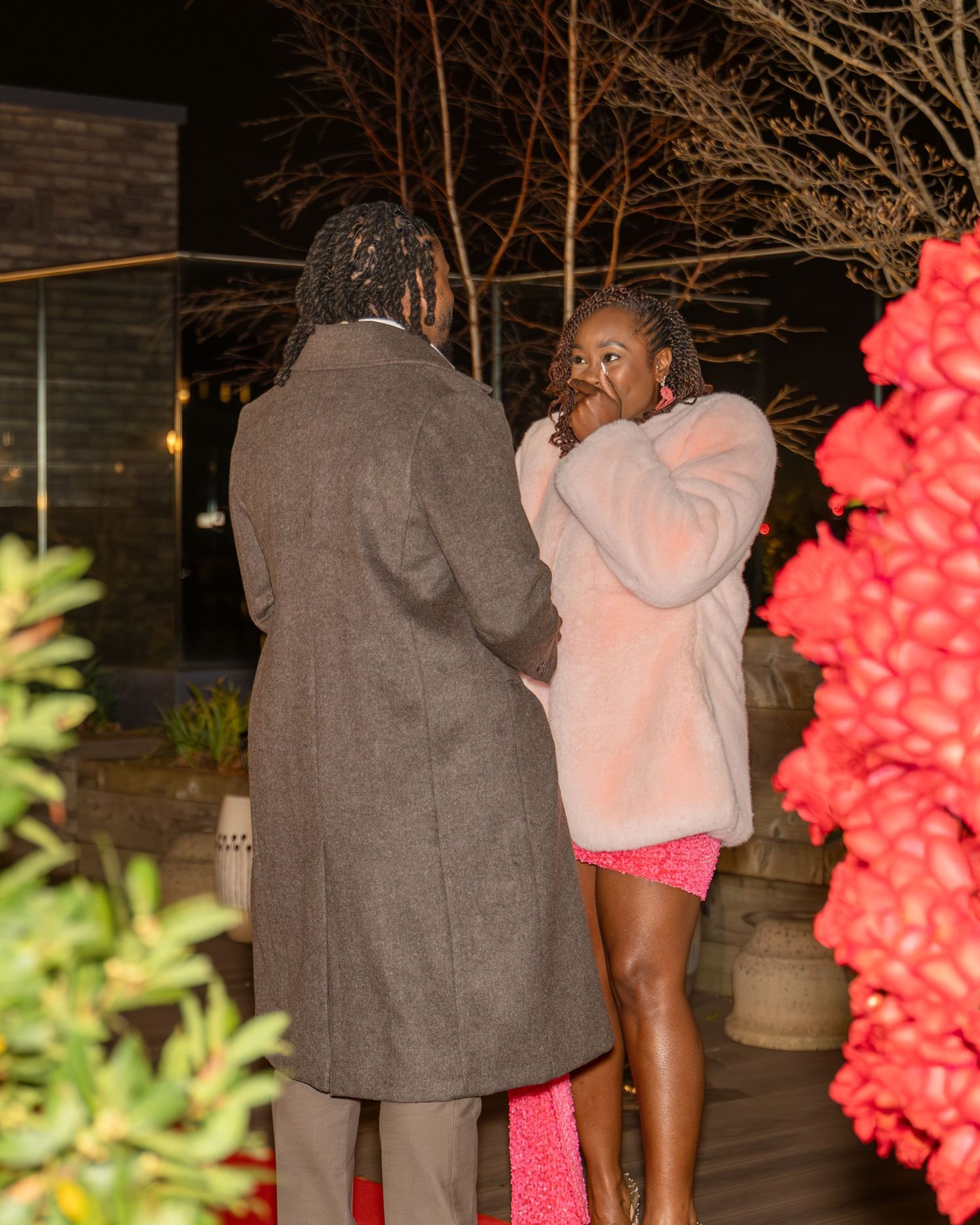 Couple stands together near red floral arrangement after emotional outdoor marriage proposal.