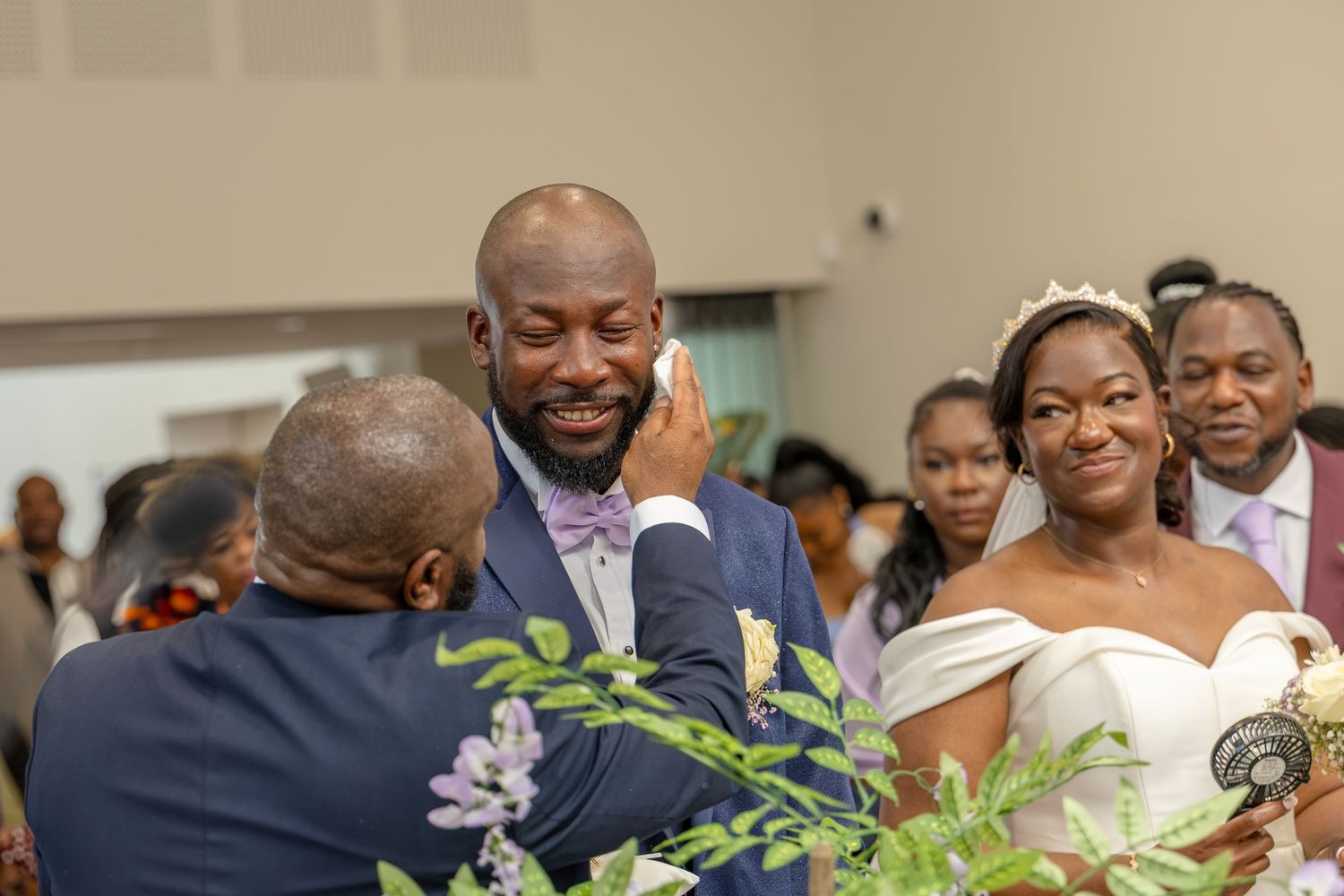Emotional groom being comforted by guest while smiling bride watches during a heartfelt wedding ceremony.