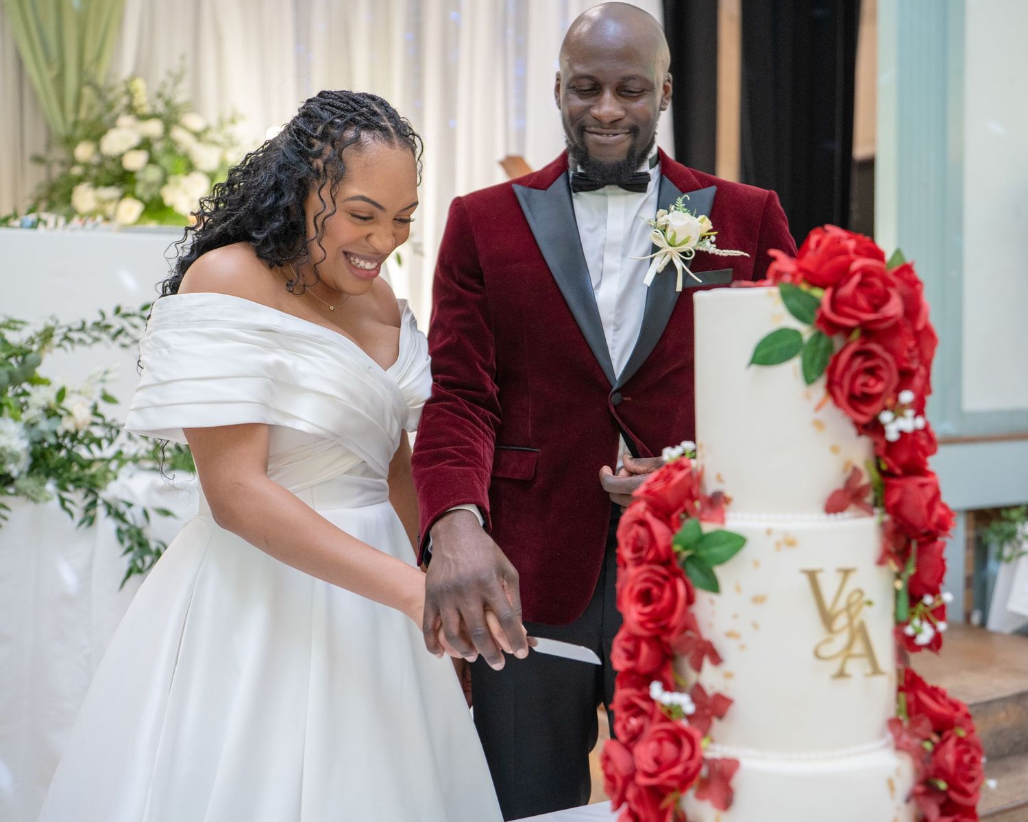 Bride and groom cutting a elegant white wedding cake adorned with red roses at their wedding reception.
