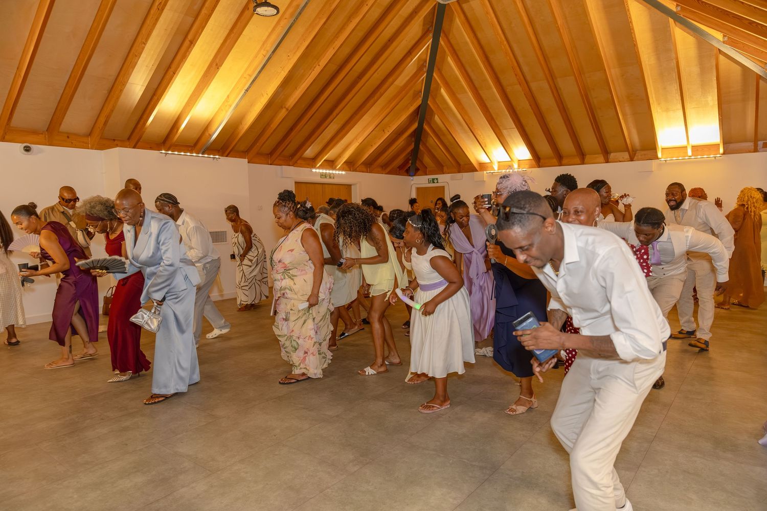 Guests dancing and celebrating at an indoor wedding reception in a wooden-roofed venue.