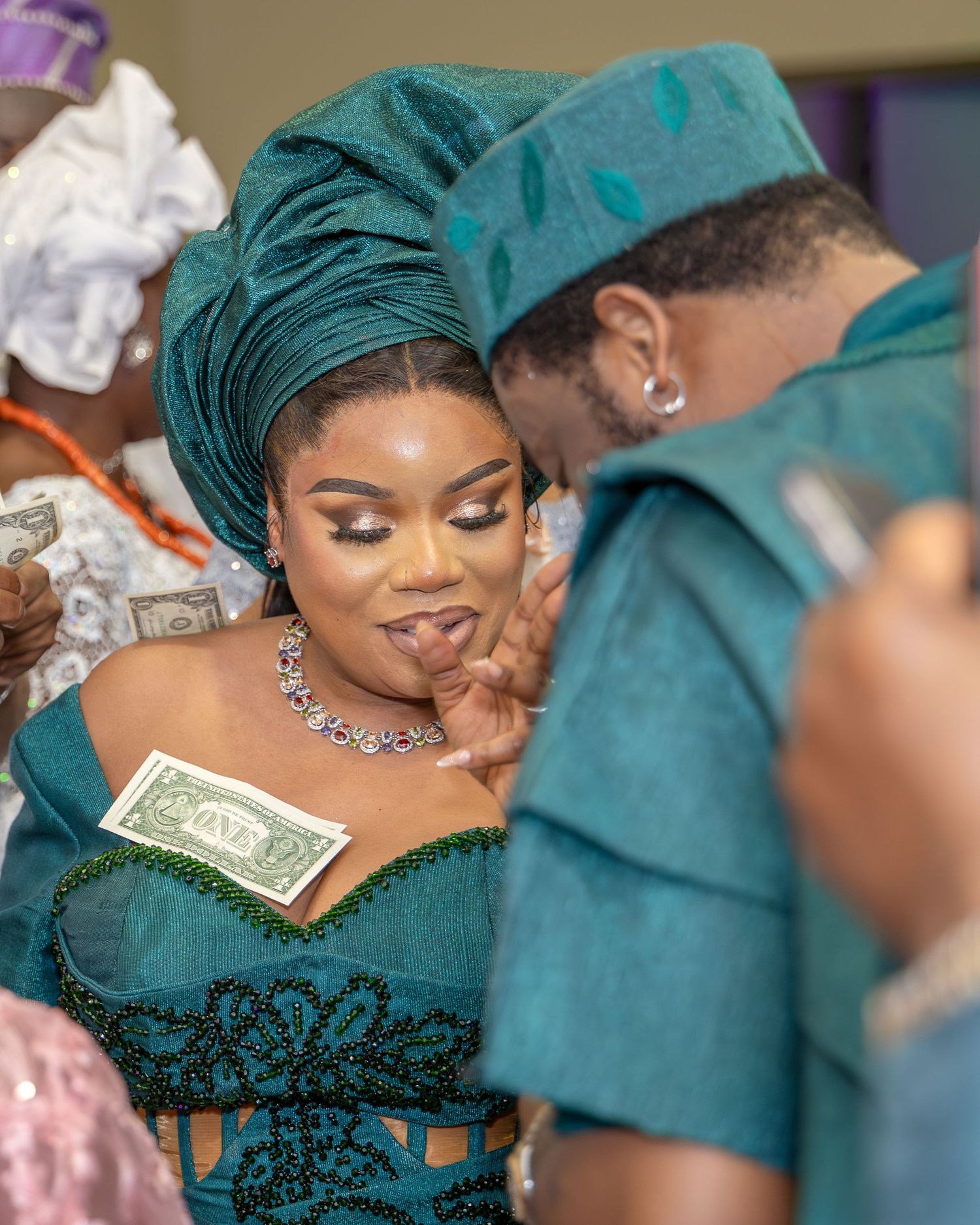 A Nigerian bride in a teal beaded corset gown and gele shares an intimate moment with her groom during their wedding.