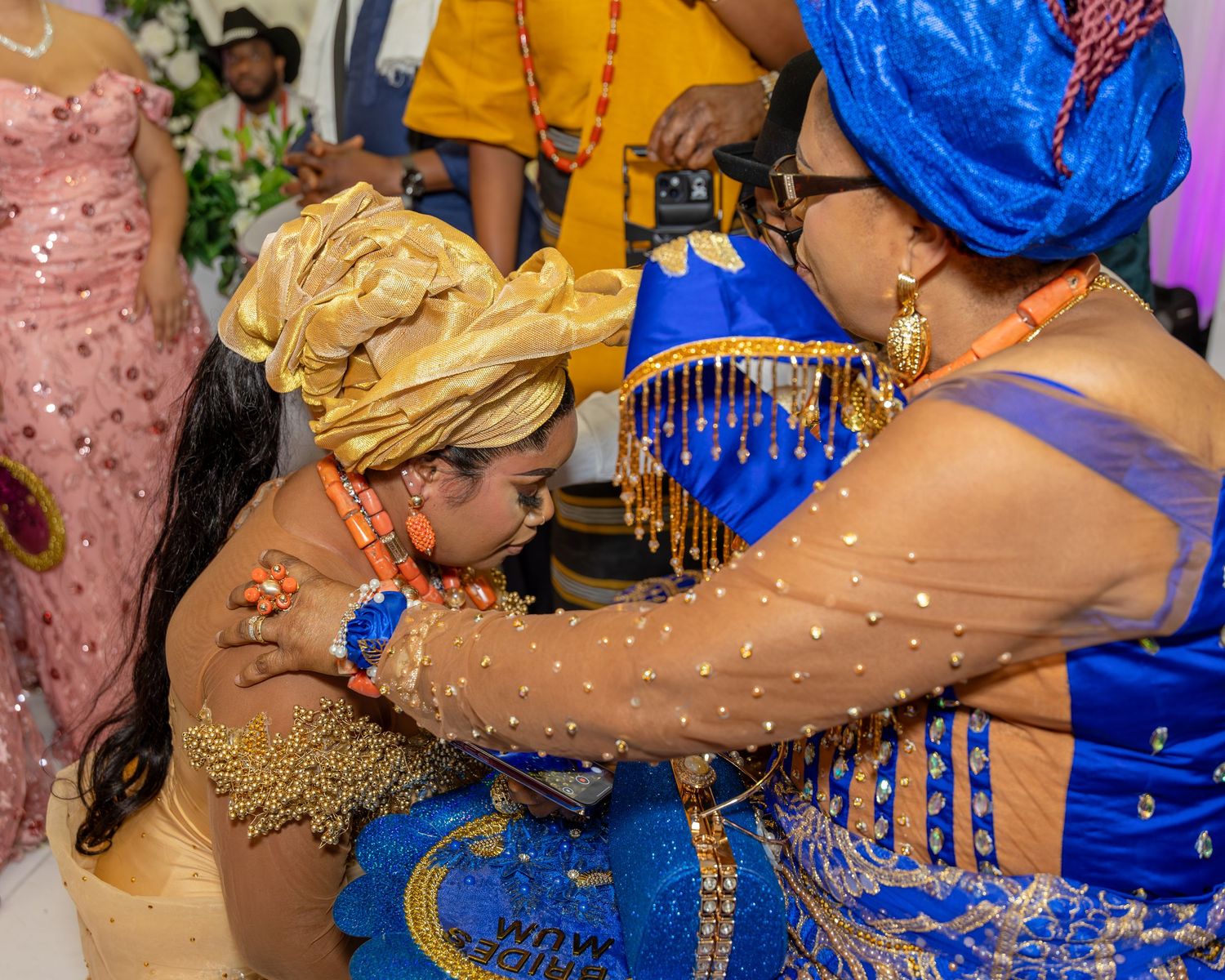 Nigerian bride bows respectfully during traditional blessing ceremony with elder in blue and gold aso-oke.