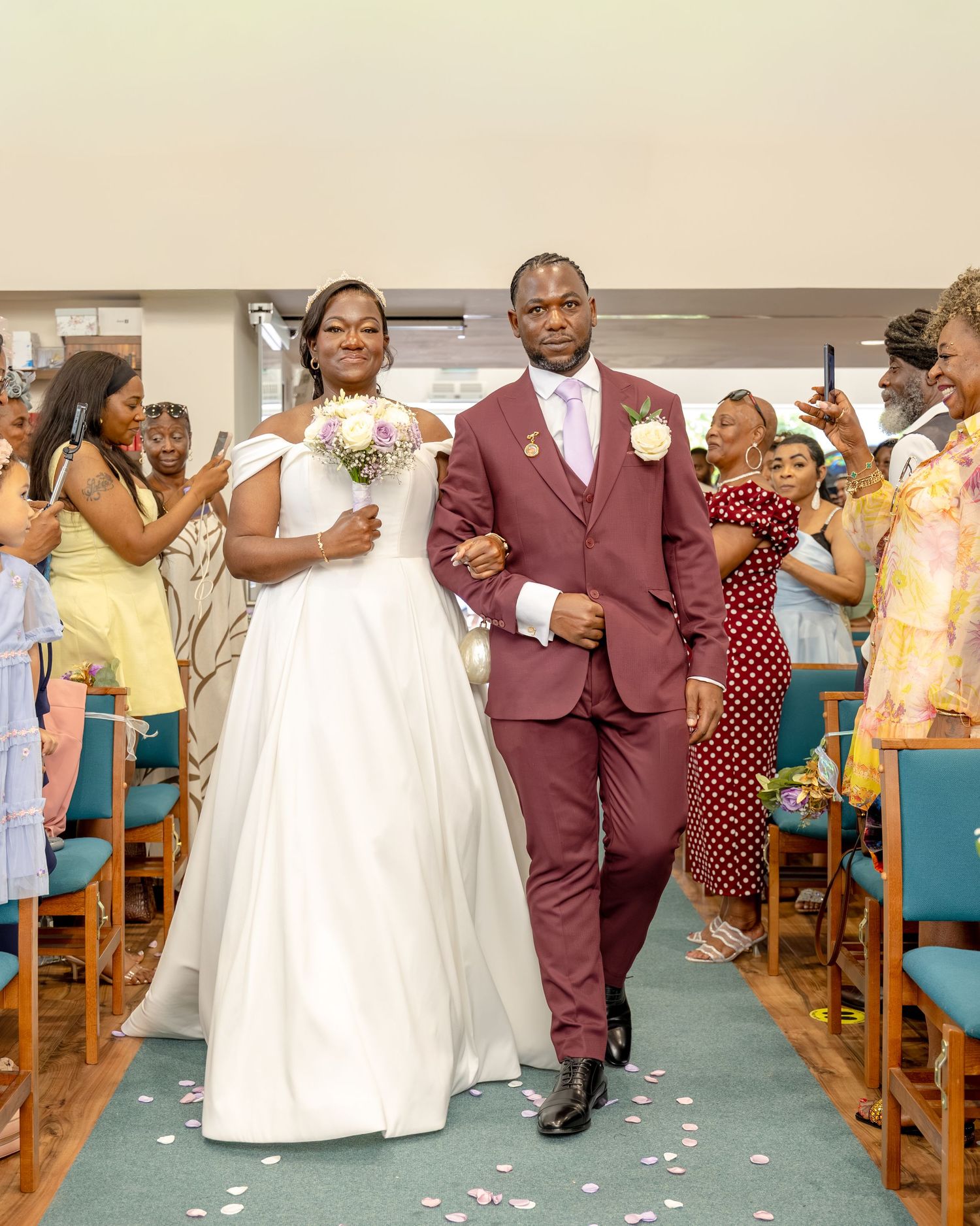 Bride and groom walk down church aisle after wedding ceremony, guests celebrating in background.