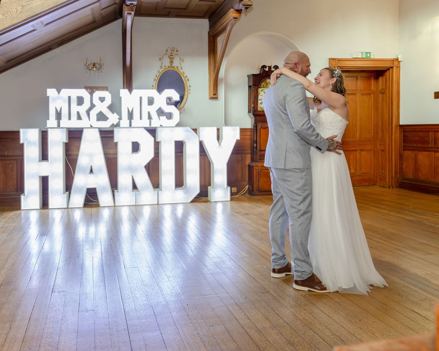 Newlyweds share first dance in front of illuminated Mr & Mrs Hardy marquee letters at elegant wedding reception venue.