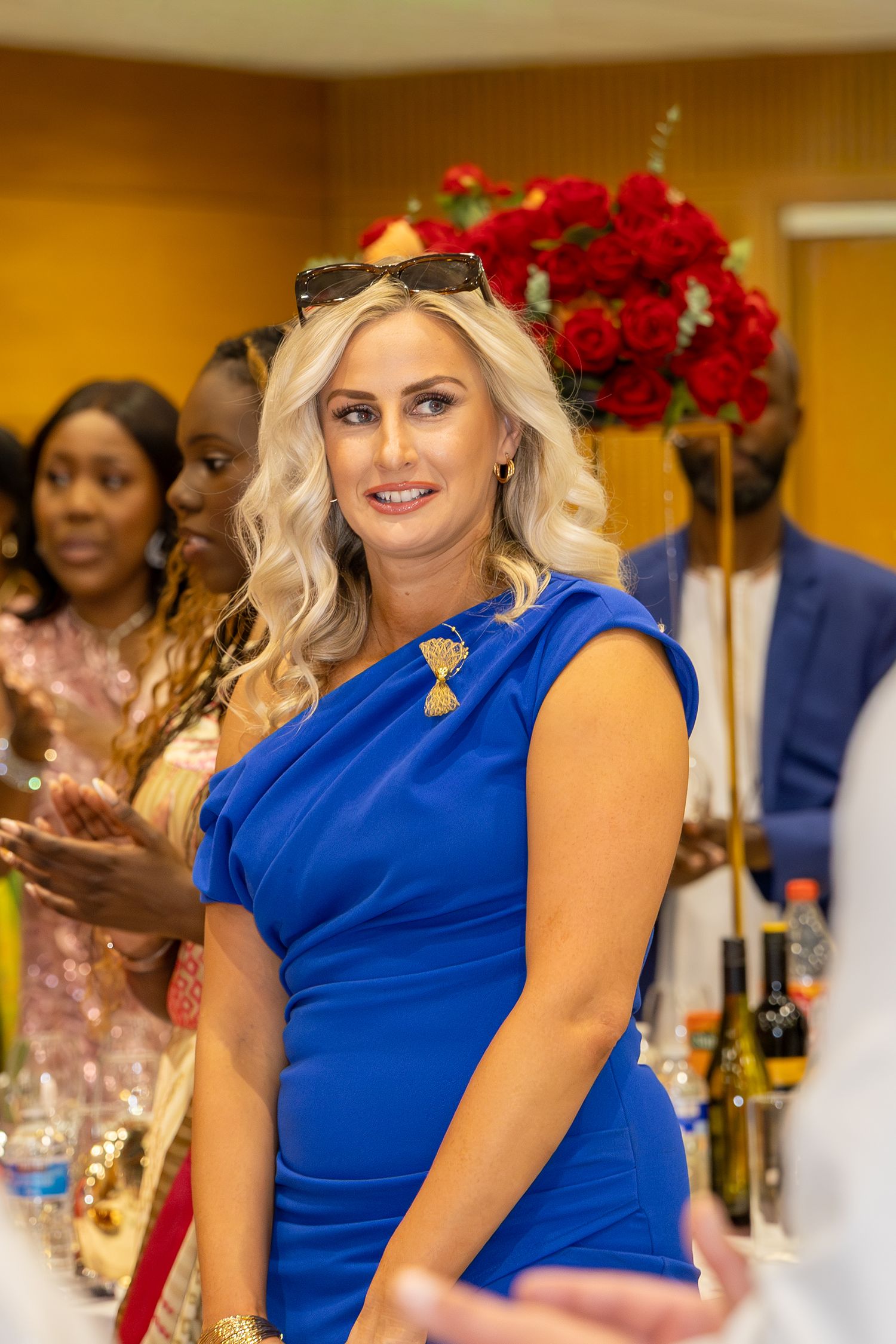 Smiling blonde woman in a royal blue dress at a wedding reception with red roses.