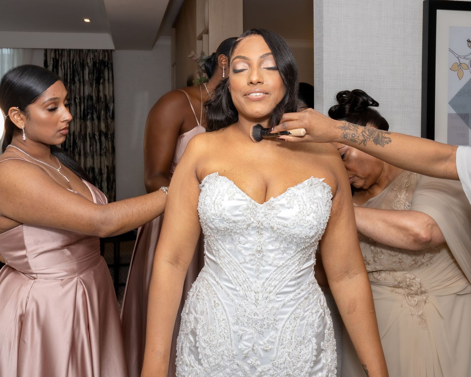 Bridesmaids in blush pink gowns help bride into her white lace strapless wedding dress.