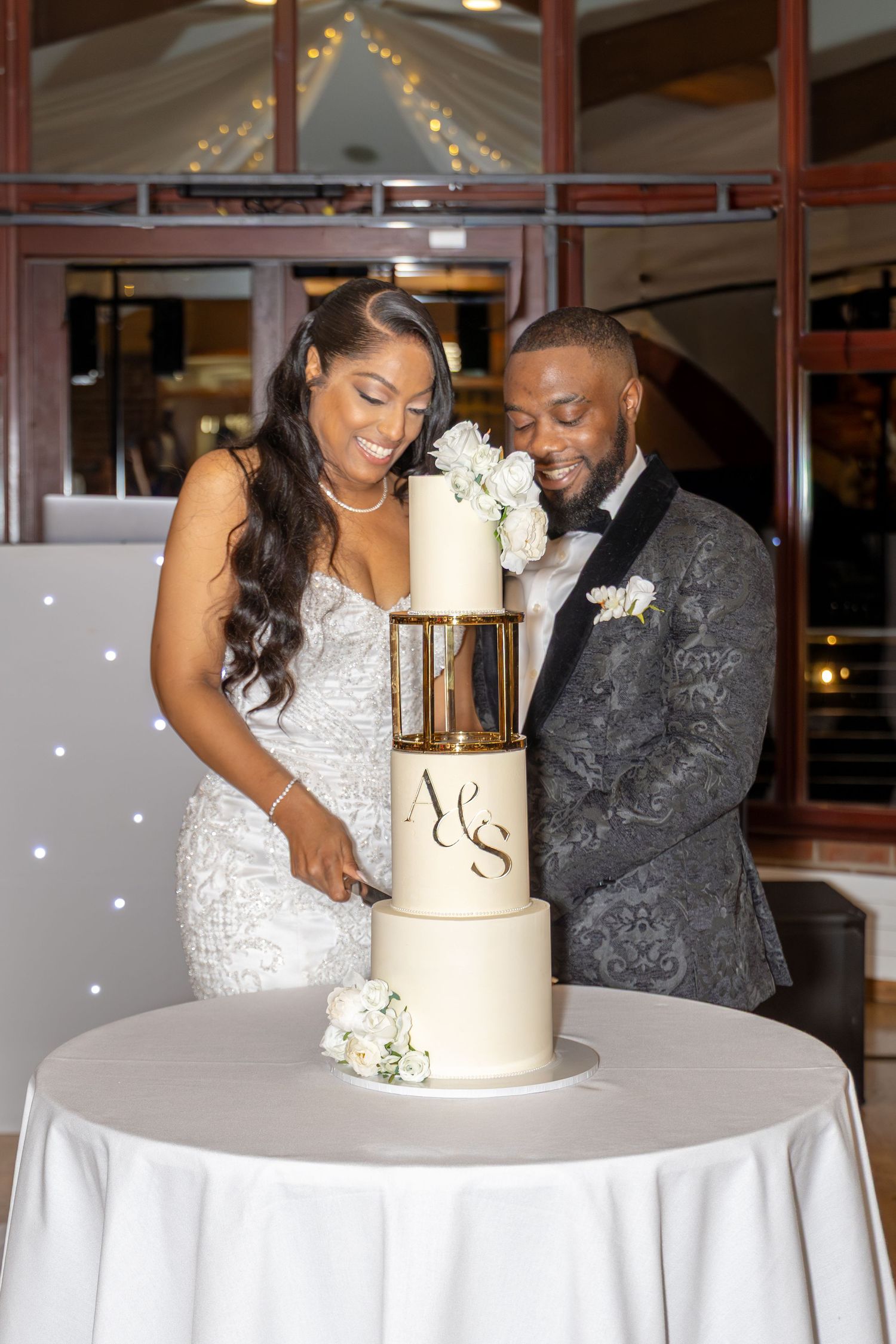 Bride and groom cut their elegant white three-tier wedding cake decorated with white flowers.