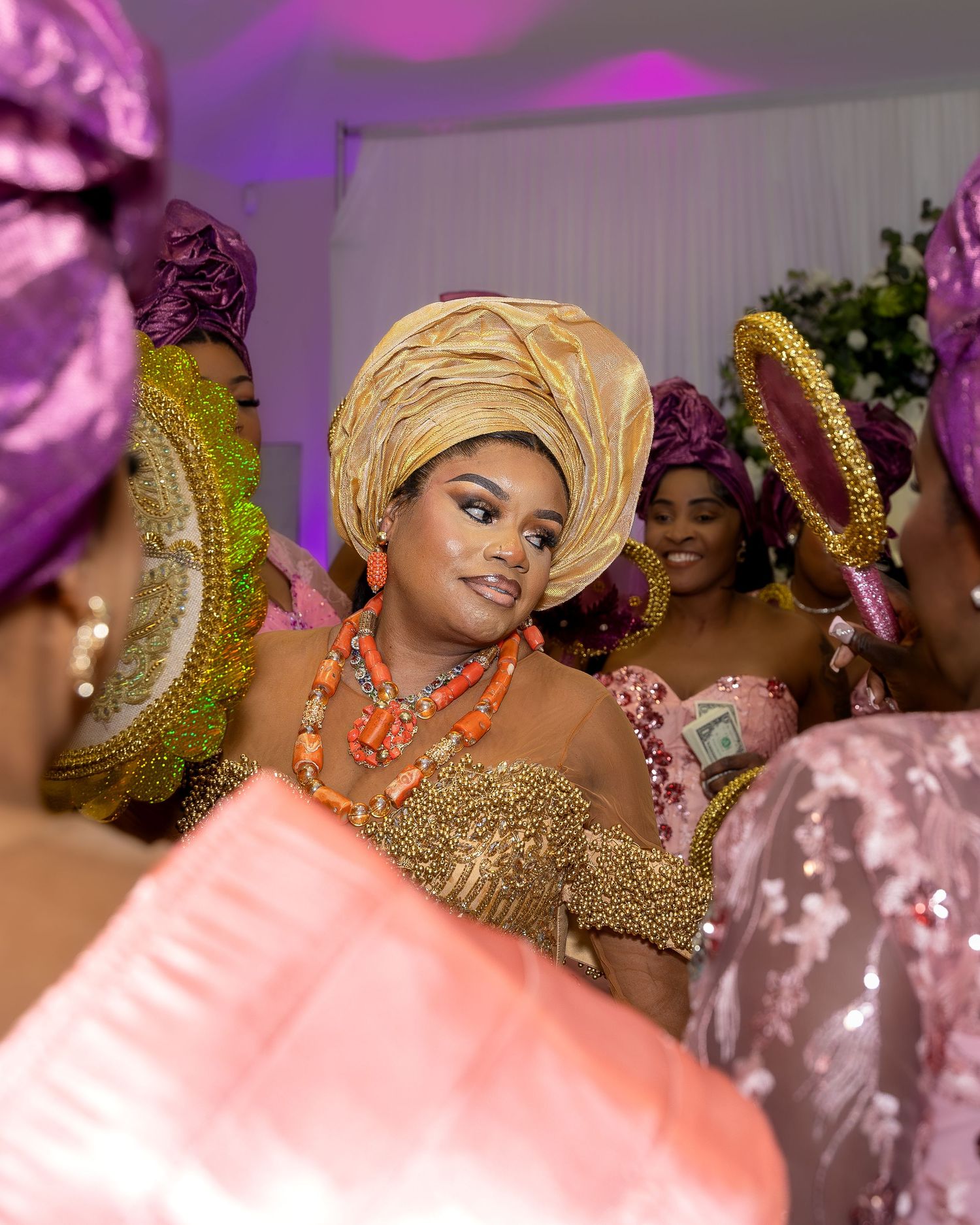 Radiant Nigerian bride in gold gele and coral jewelry smiles during traditional wedding ceremony celebration.