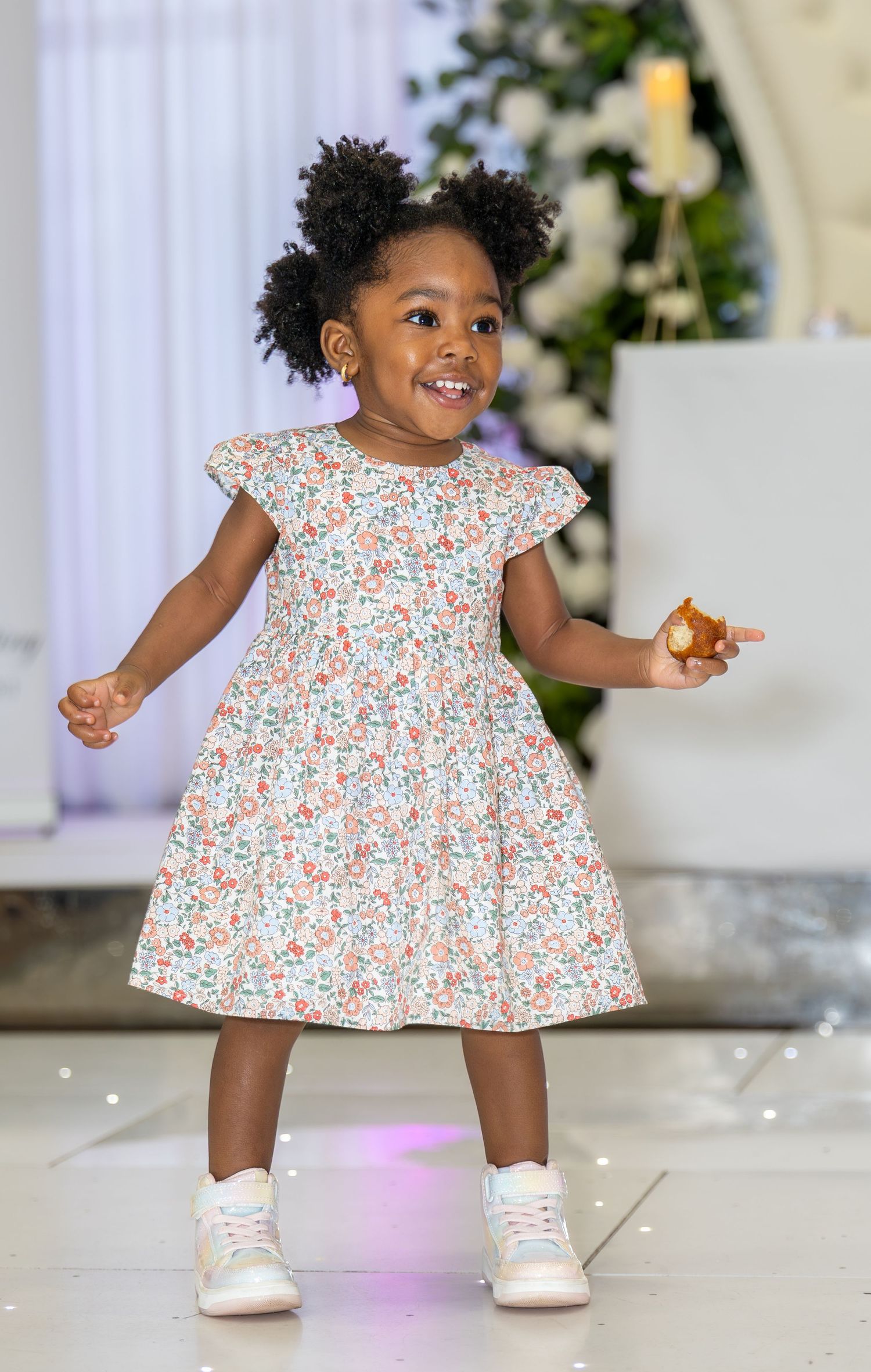 Adorable toddler girl in floral dress dancing joyfully at a wedding celebration venue.