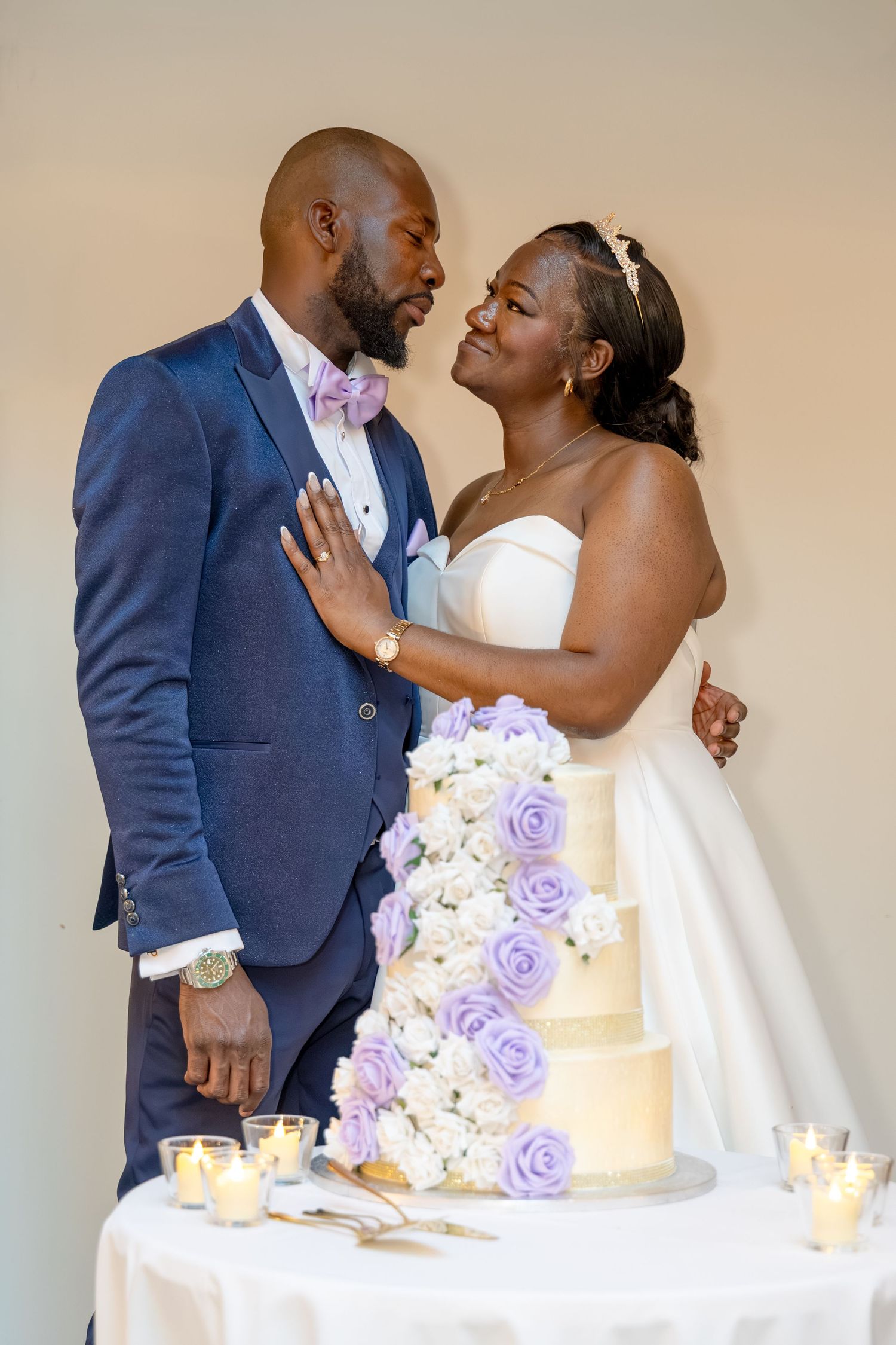 Newlywed couple sharing a romantic moment beside a elegant tiered wedding cake with purple and white roses.