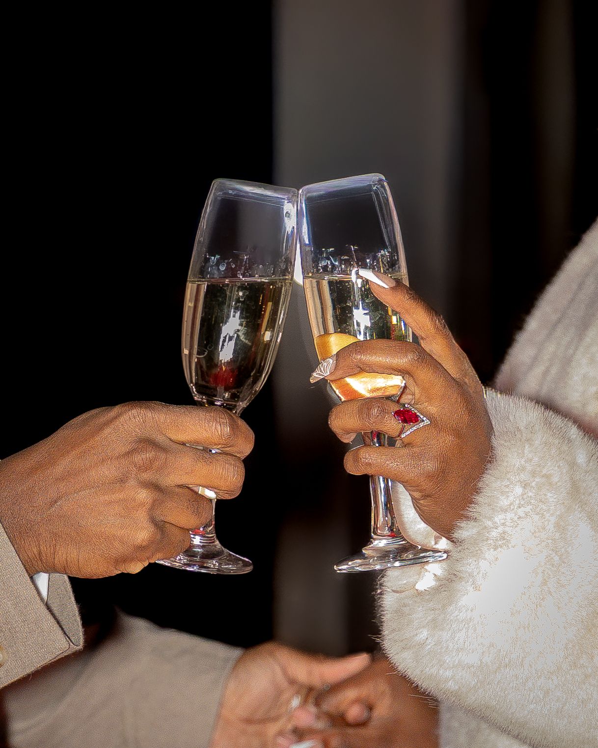 Two hands clinking champagne glasses in a celebratory toast at a romantic event.