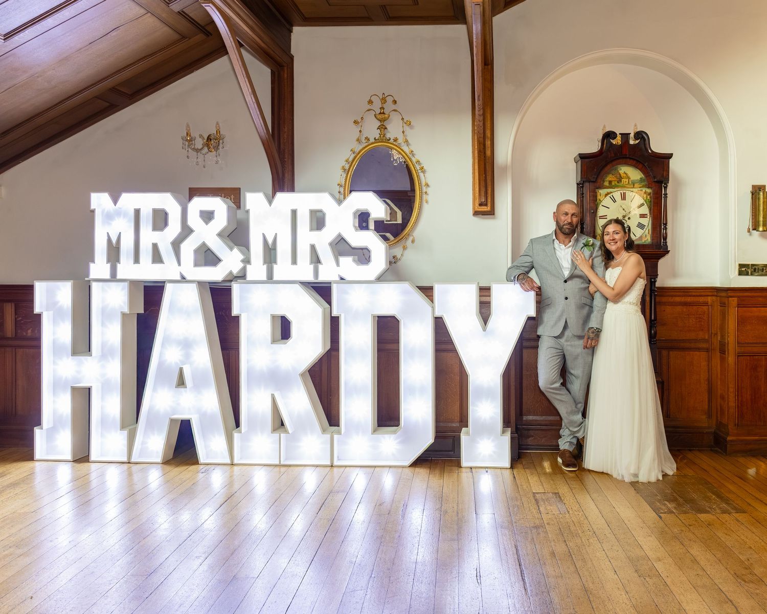 Newlyweds Mr & Mrs Hardy pose beside illuminated marquee letter signs at their elegant wedding venue.