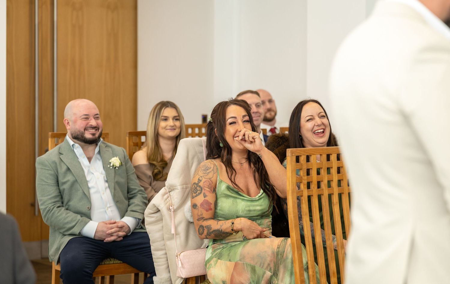 Wedding guests laugh and smile joyfully while seated during a wedding ceremony in a modern venue.