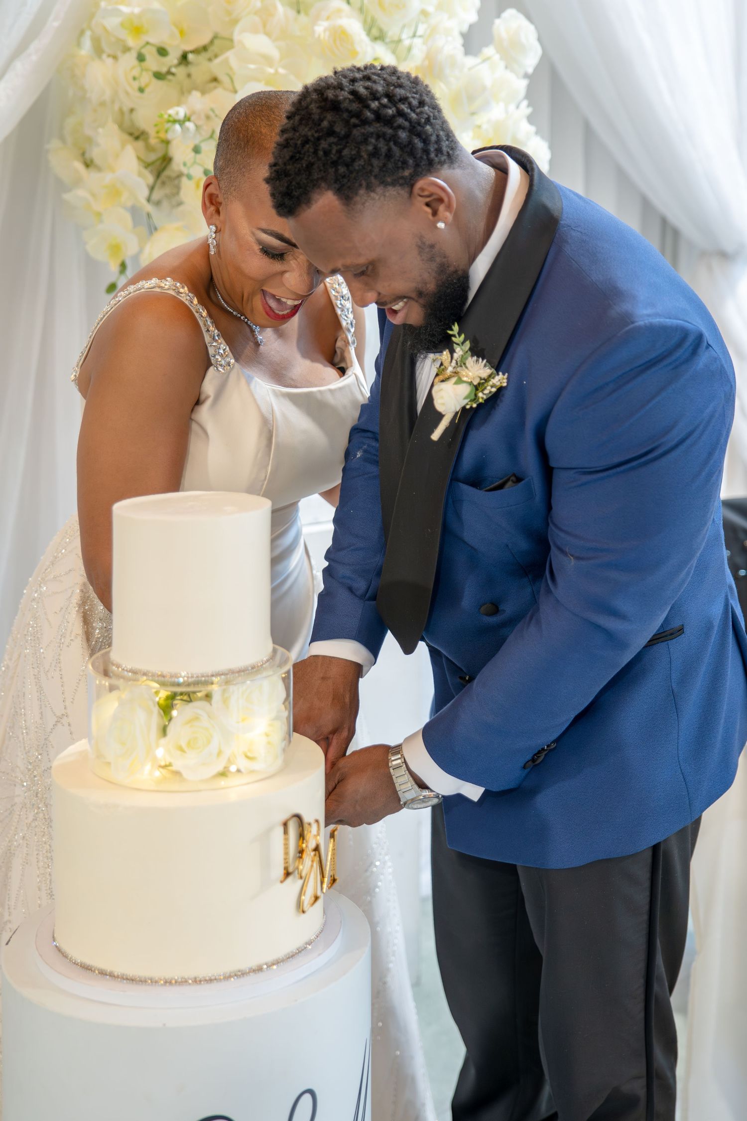 Bride and groom cutting their elegant white three-tier wedding cake adorned with roses at their wedding reception.