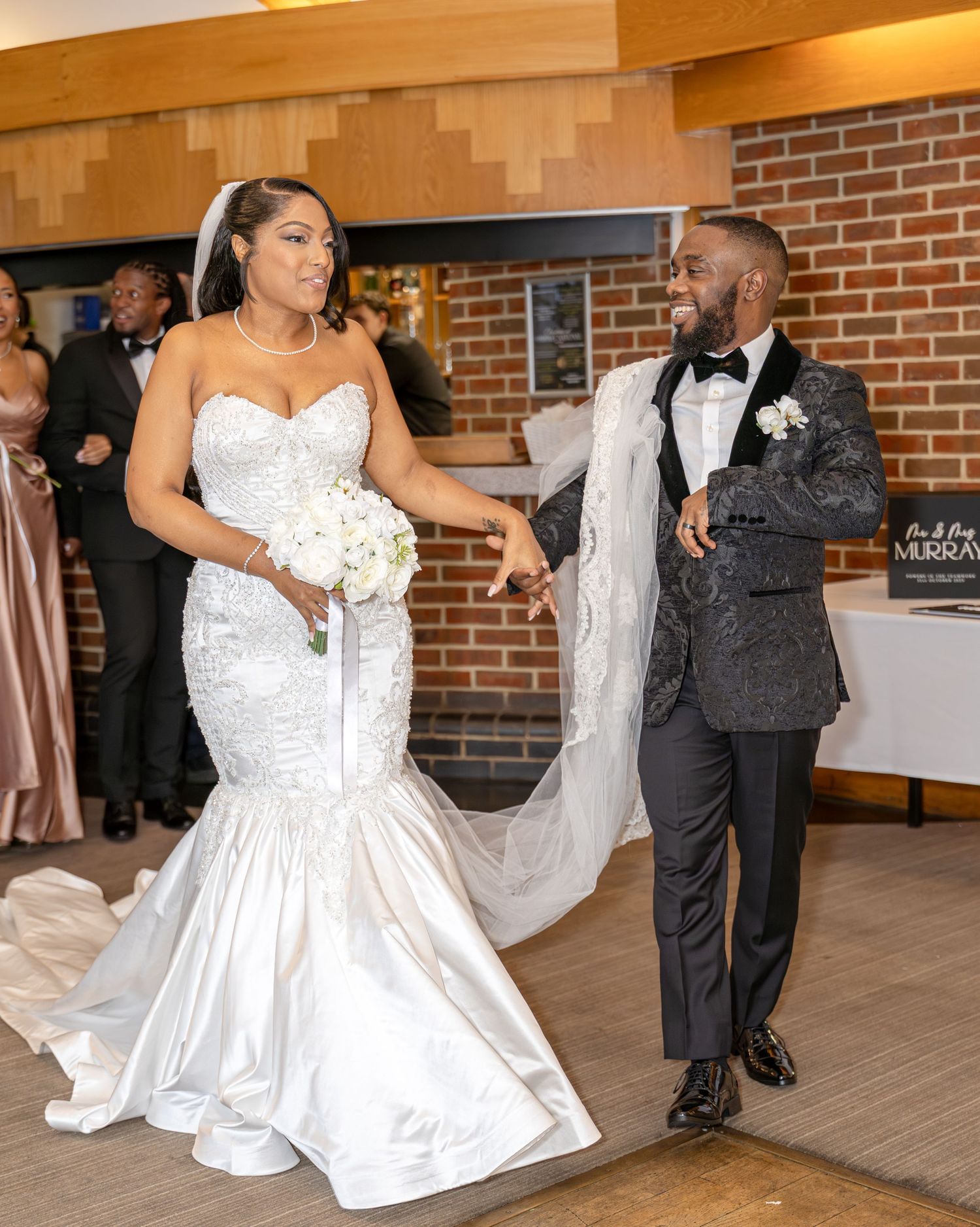 Bride in mermaid wedding gown and groom in black tuxedo dancing at wedding reception.