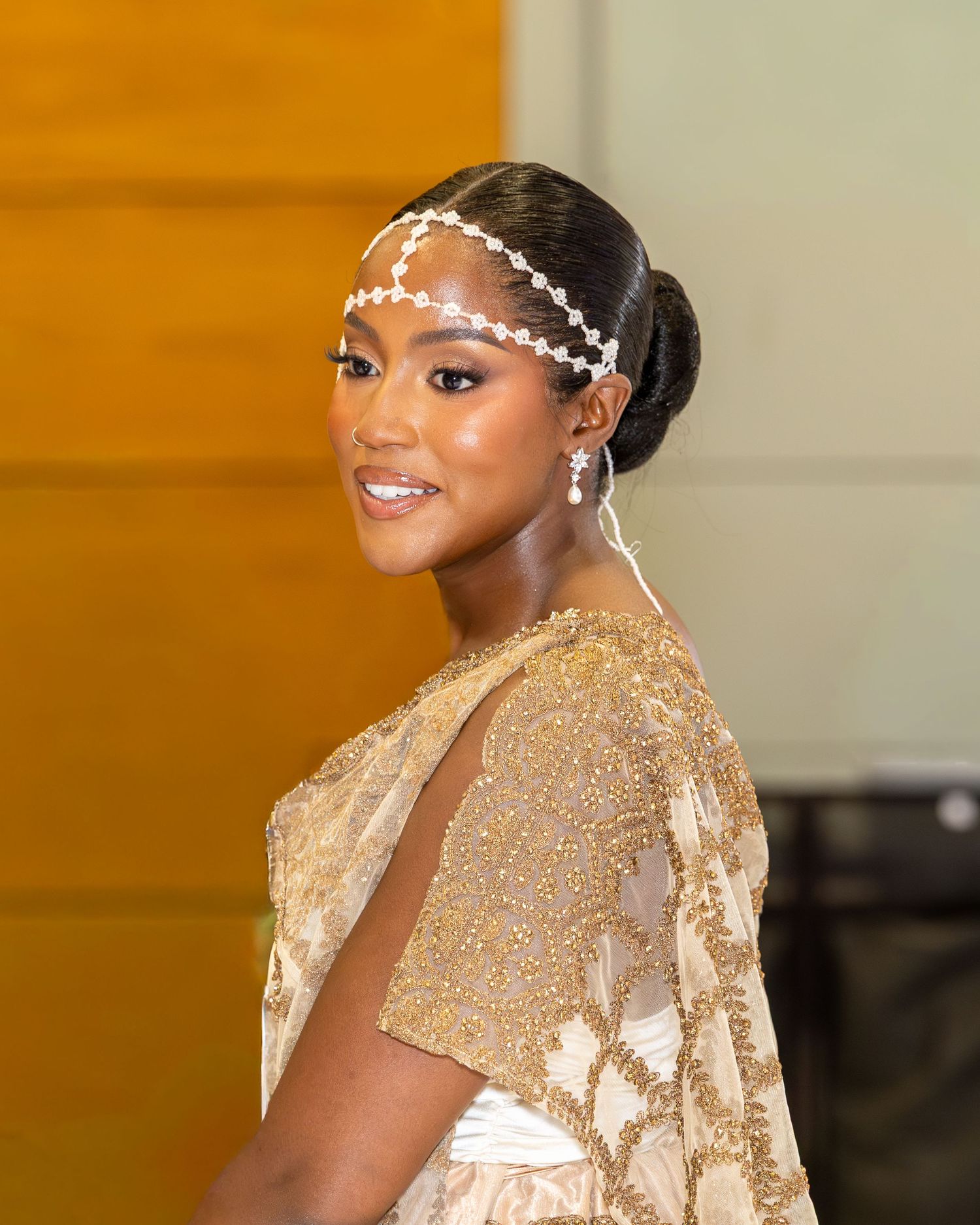 Beautiful bride with elegant updo and pearl chain headpiece wearing gold beaded gown at wedding.