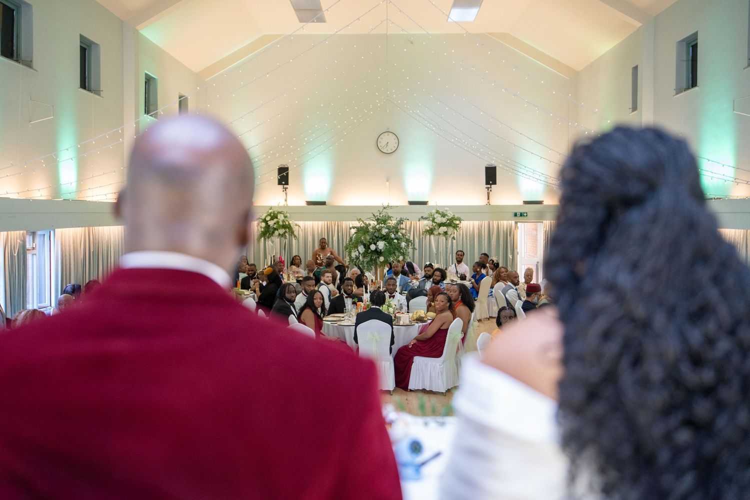 Elegant banquet hall event with guests seated at round tables, viewed from behind two attendees in formal attire.