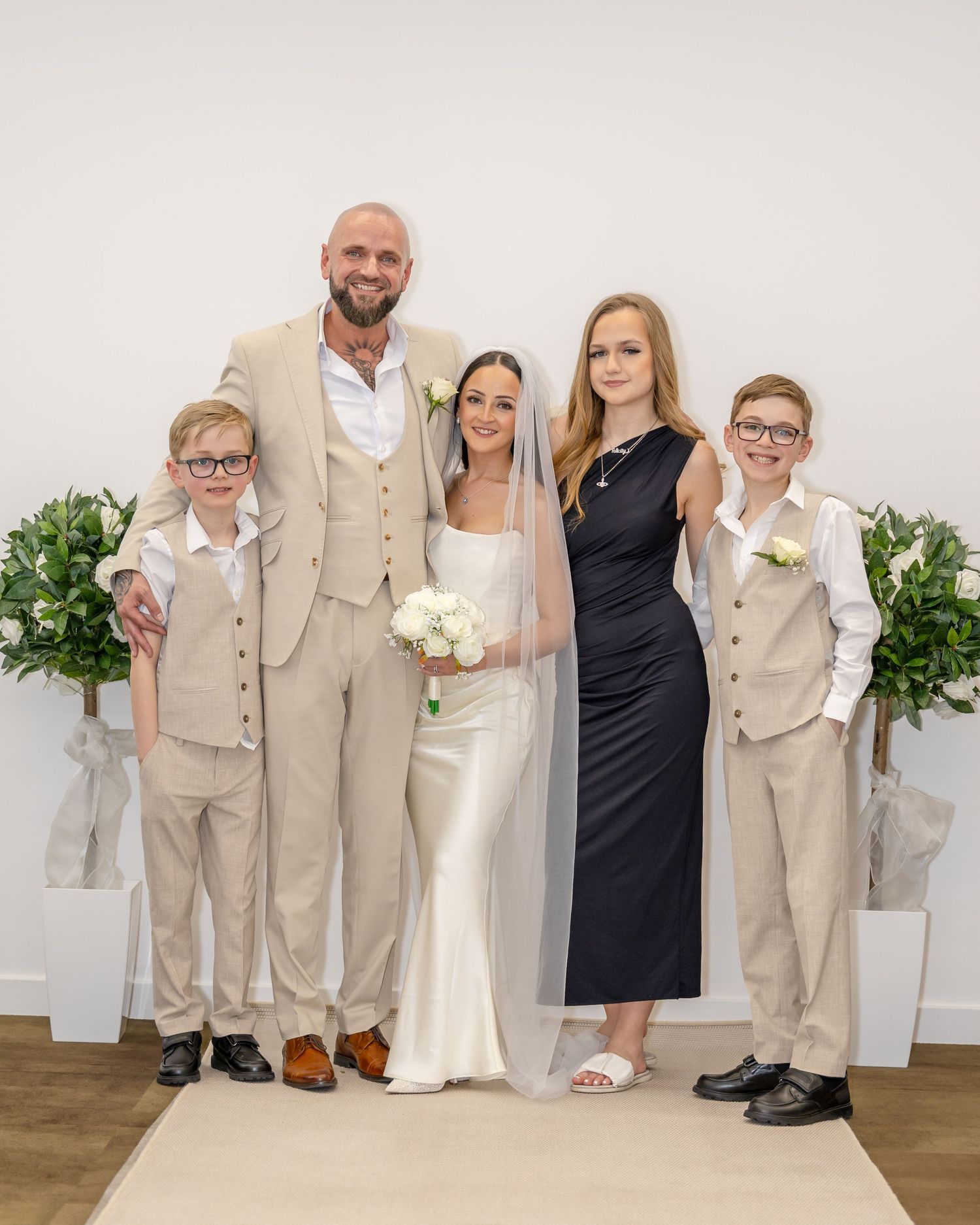 Wedding couple posing with three children in formal attire at a bright ceremony venue.