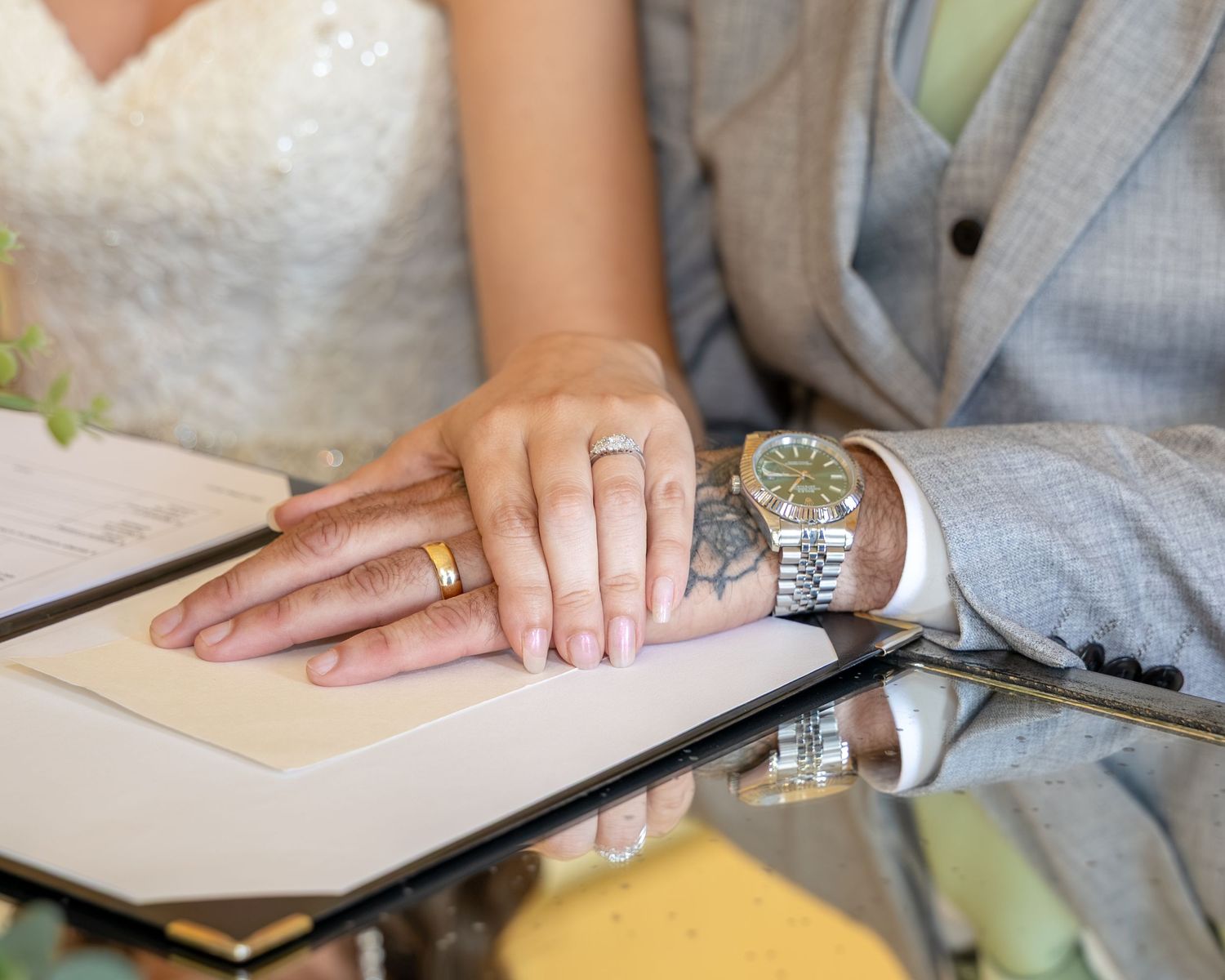 Bride and groom hands with wedding rings resting on marriage certificate during wedding ceremony.