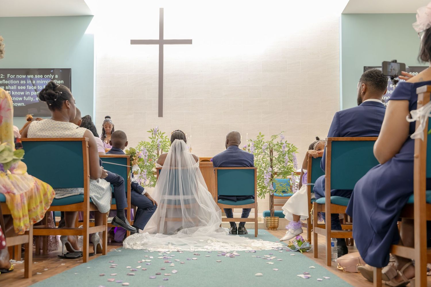 A bride and groom sit at the altar of a church during their wedding ceremony, with guests seated in pews on either side.