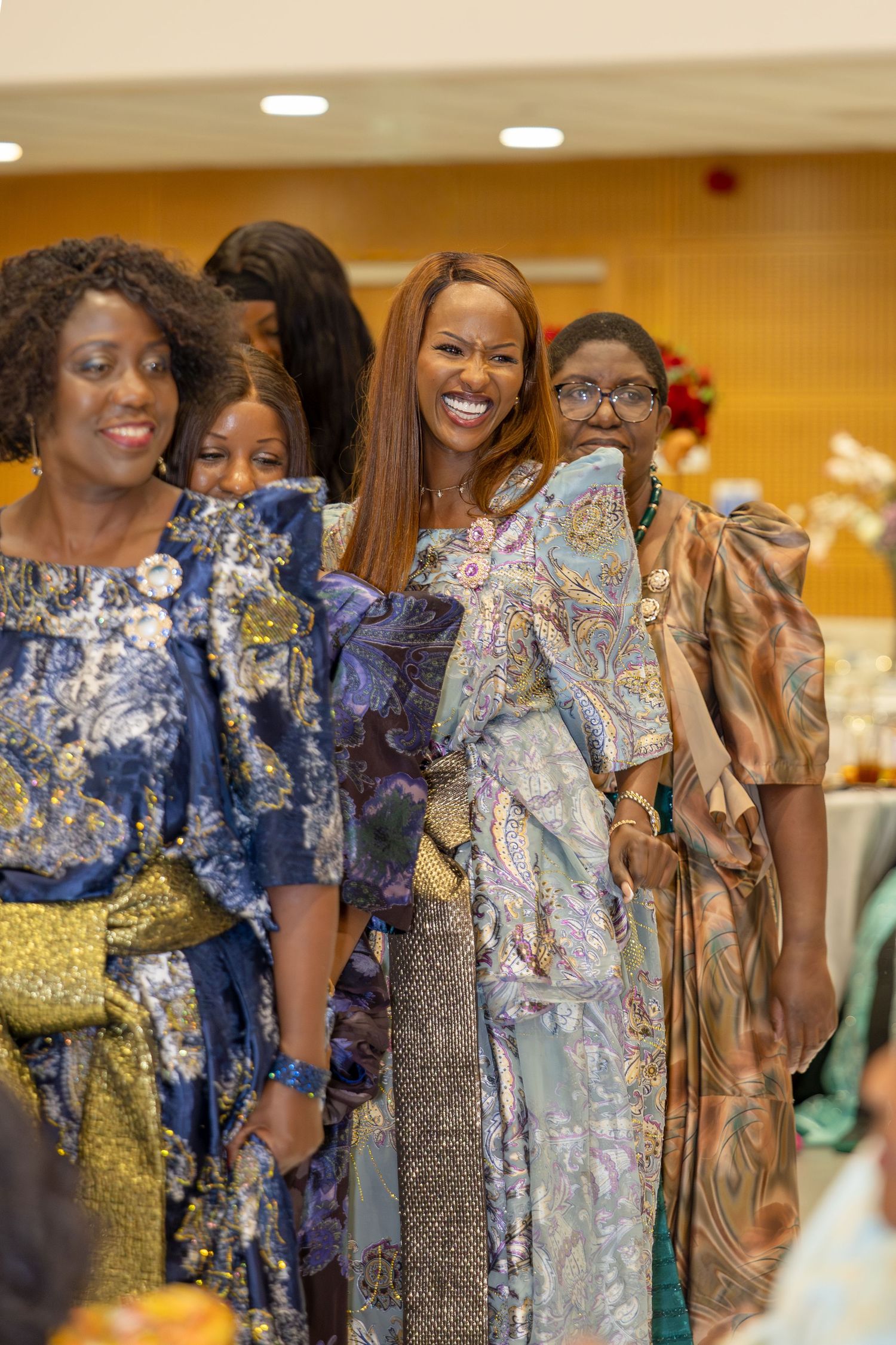 Women in vibrant African traditional attire smile and pose together at an elegant cultural celebration event.
