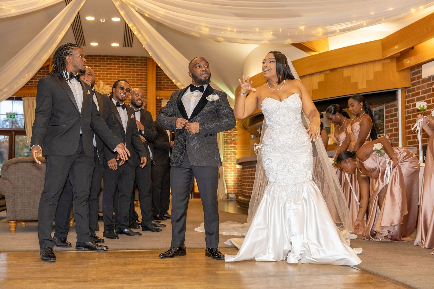 Groom in patterned tuxedo jacket shares a joyful moment with bride in white mermaid gown at reception.