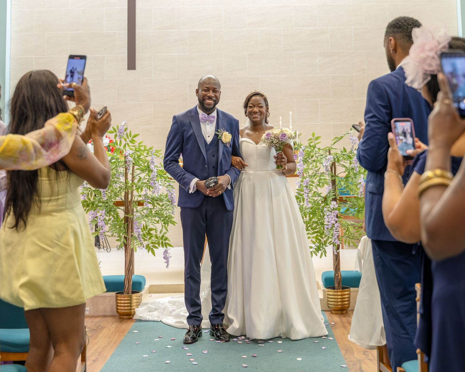 Joyful newlywed couple walks down church aisle as guests photograph the wedding ceremony celebration.