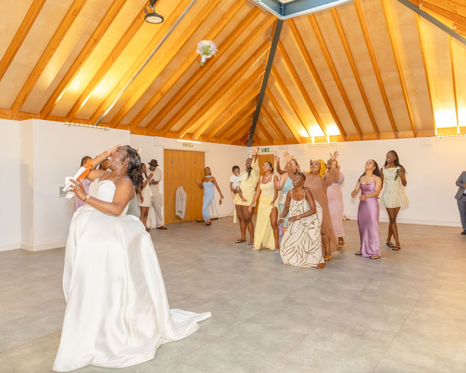 Bride tosses bouquet to bridesmaids in colorful dresses inside a wooden chapel at a wedding reception.