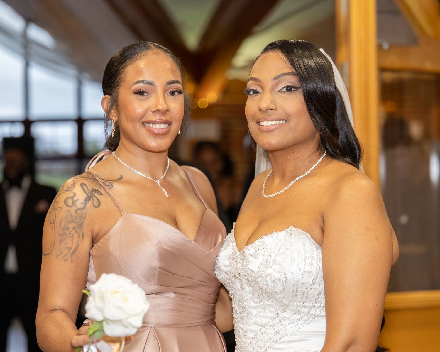 Bride in strapless lace gown posing with bridesmaid in champagne dress at wedding.
